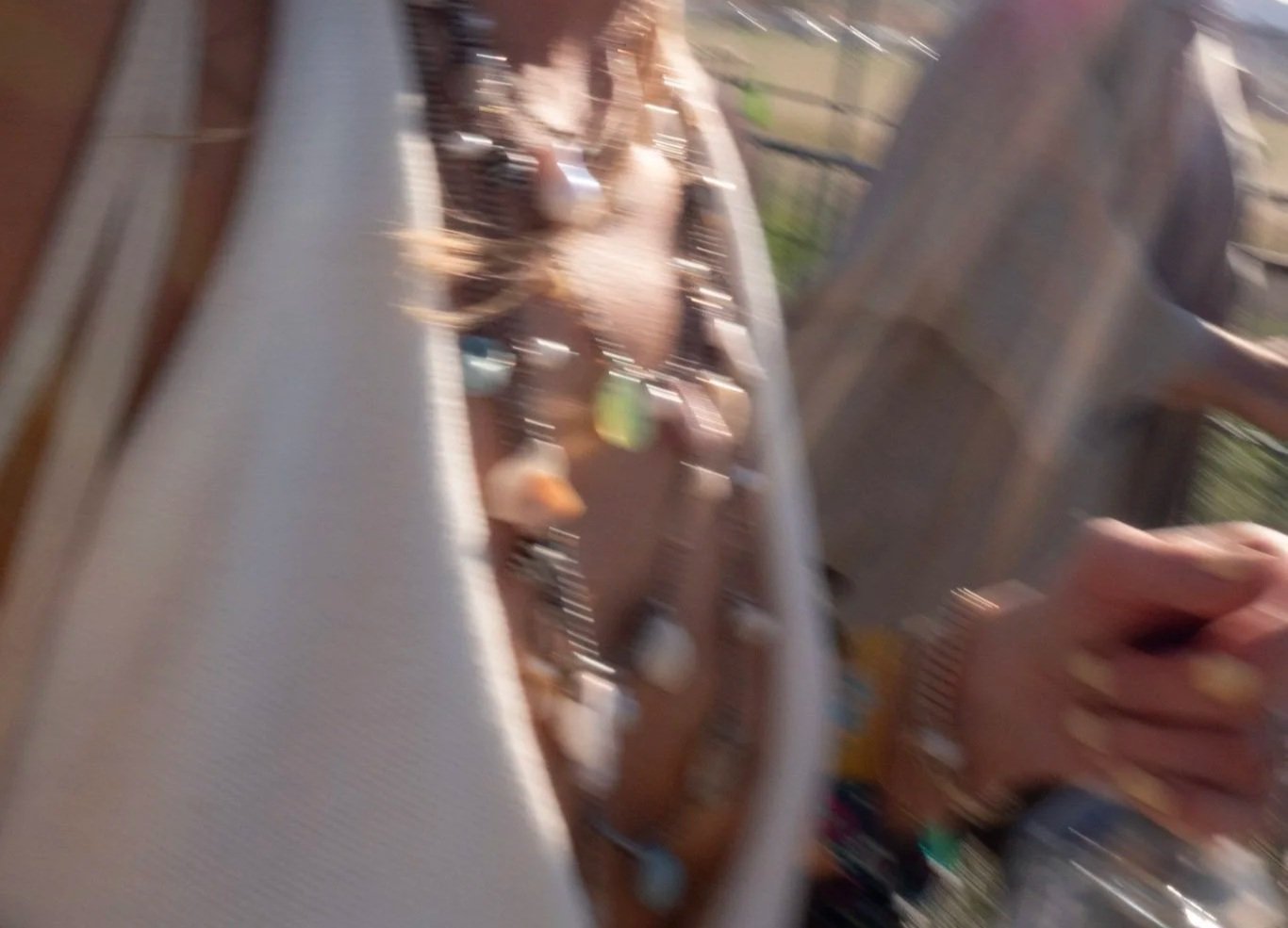 Blurry photo of a barbecue grill on a balcony with cooking utensils and food, with a hand holding a glass in the foreground.