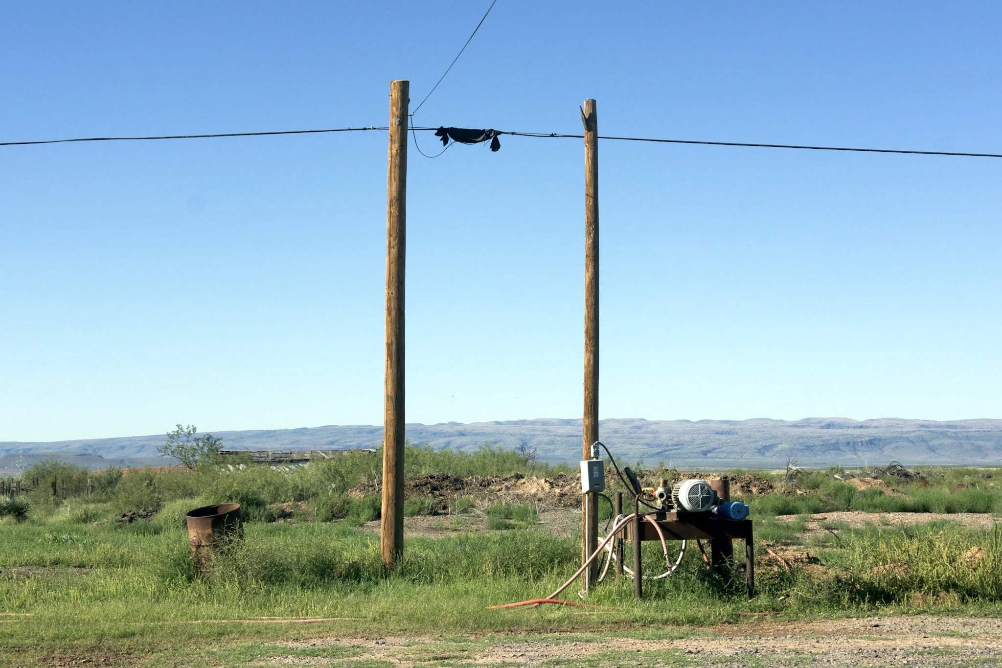 Wooden utility poles with attached electrical equipment and wires in a rural landscape under a clear blue sky.