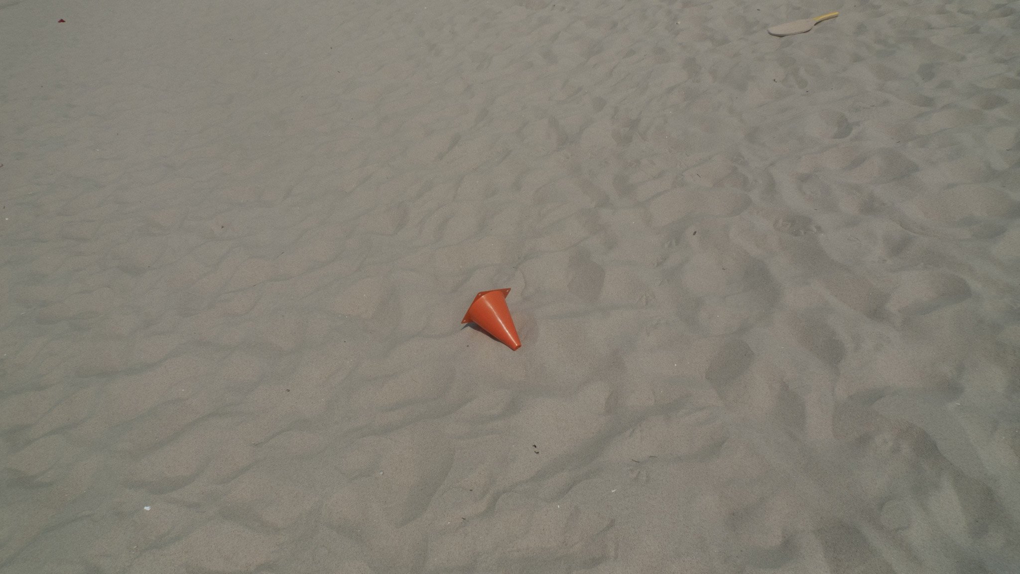 A small orange traffic cone lying on its side on a sandy surface.
