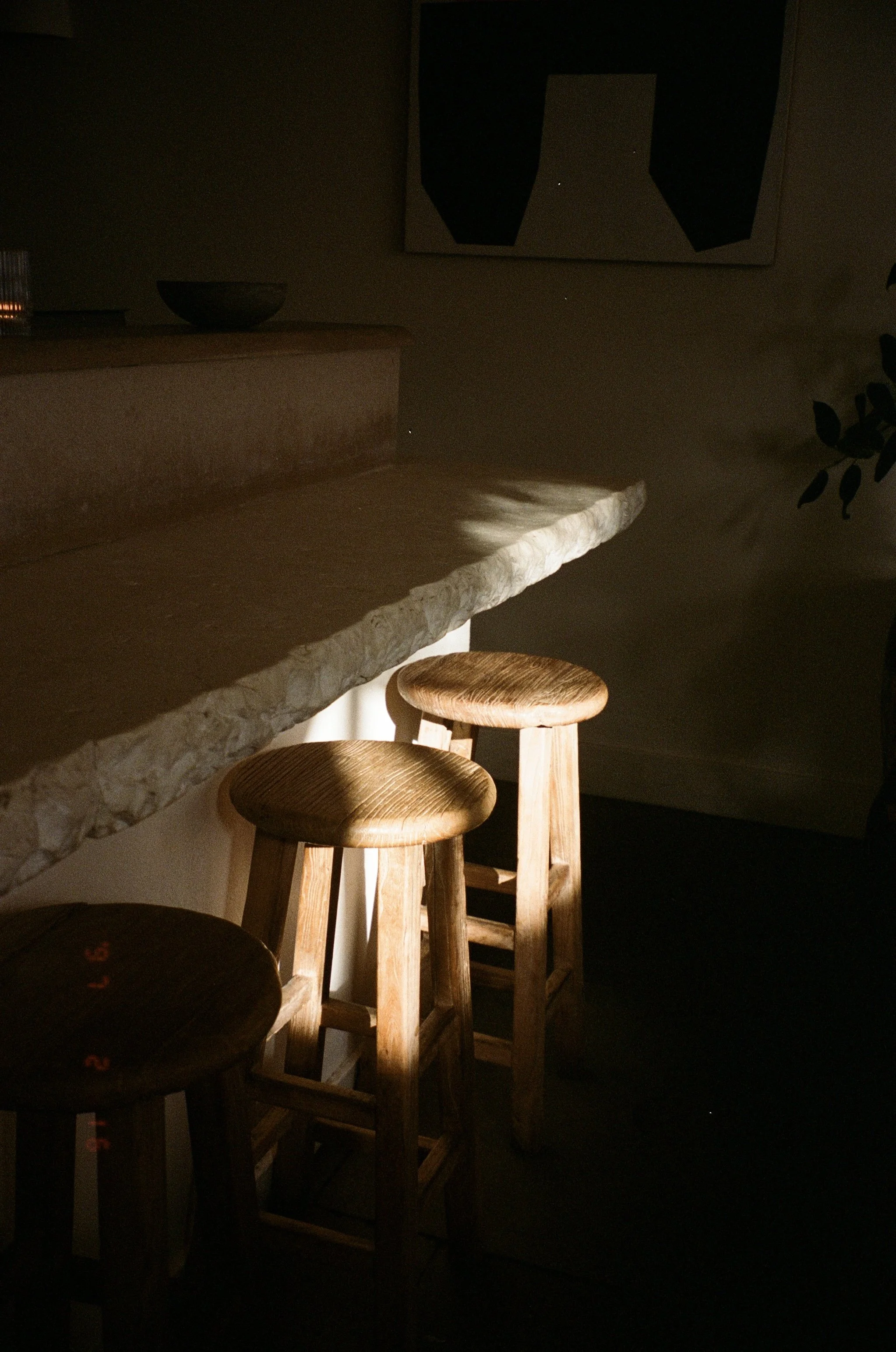 Dimly lit kitchen bar area with wooden stools, a stone countertop, and wall art hanging above.