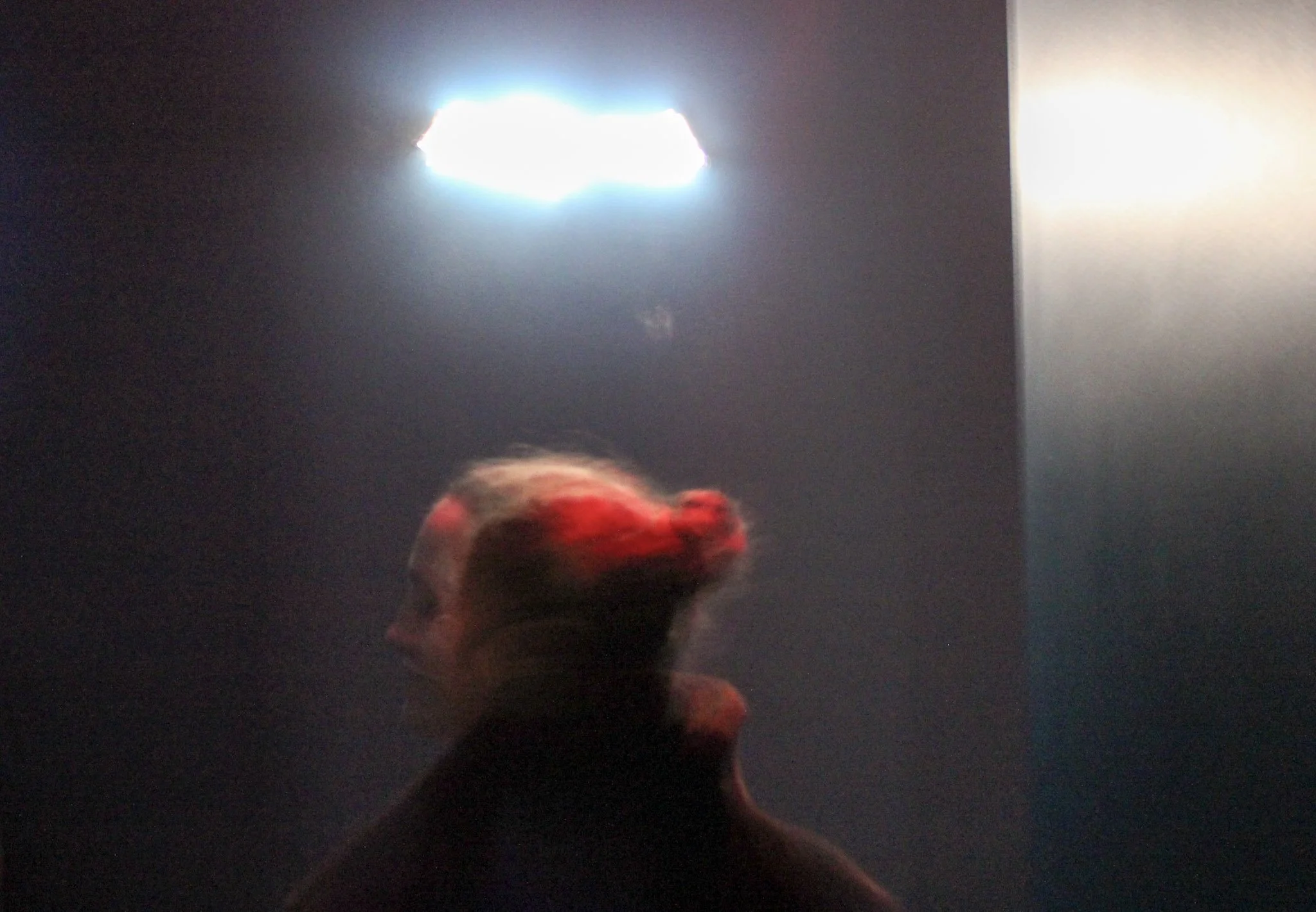A blurry image of a person with red hair in front of a dark background with a bright, glowing light source in the top center.