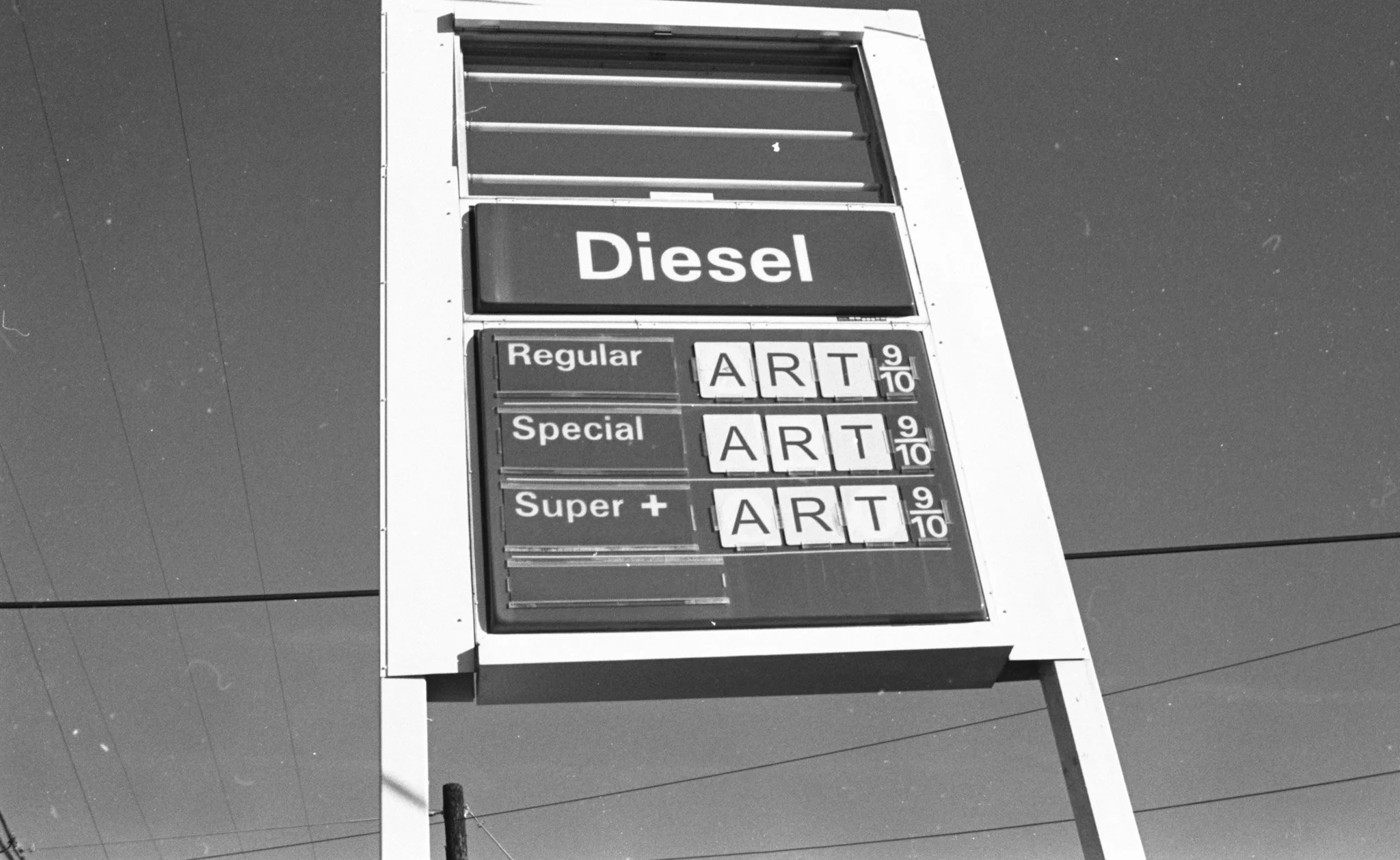 A black and white photo of a gas station price sign showing prices for Diesel, Regular, Special, and Super +ART fuel types. The Diesel price is prominently displayed.
