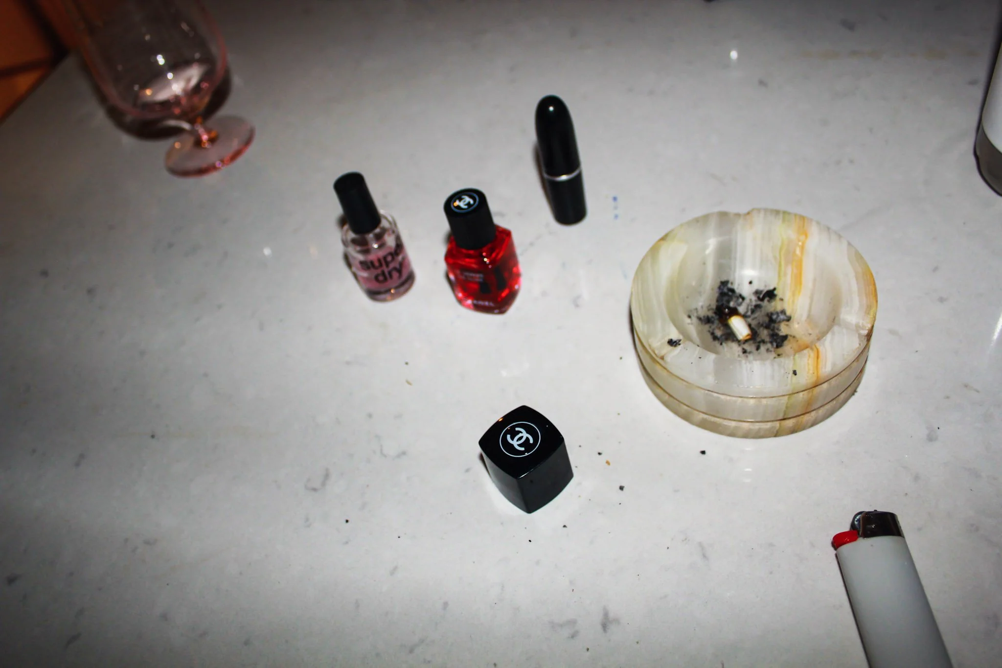 Collection of nail polish bottles, a shell-shaped ashtray with cigarette ashes, and a lighter on a white surface.