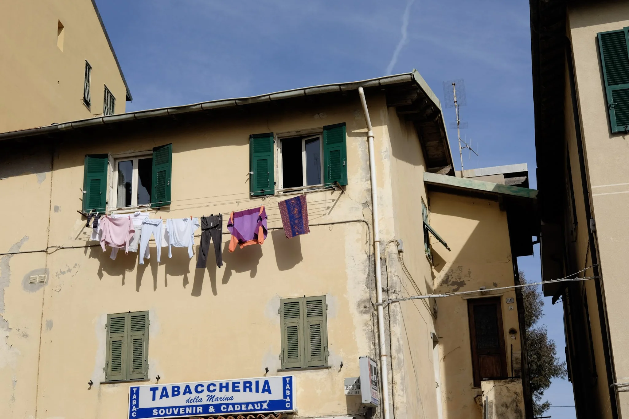 Building with green window shutters, laundry hanging outside, and a sign that reads 'Tabaccheria della Marina, Souvenir & Cadeaux' in Italian.