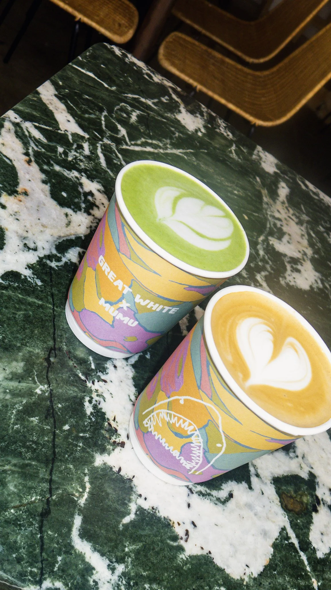 Two colorful cups with matcha and caramel drinks on a green marble table.