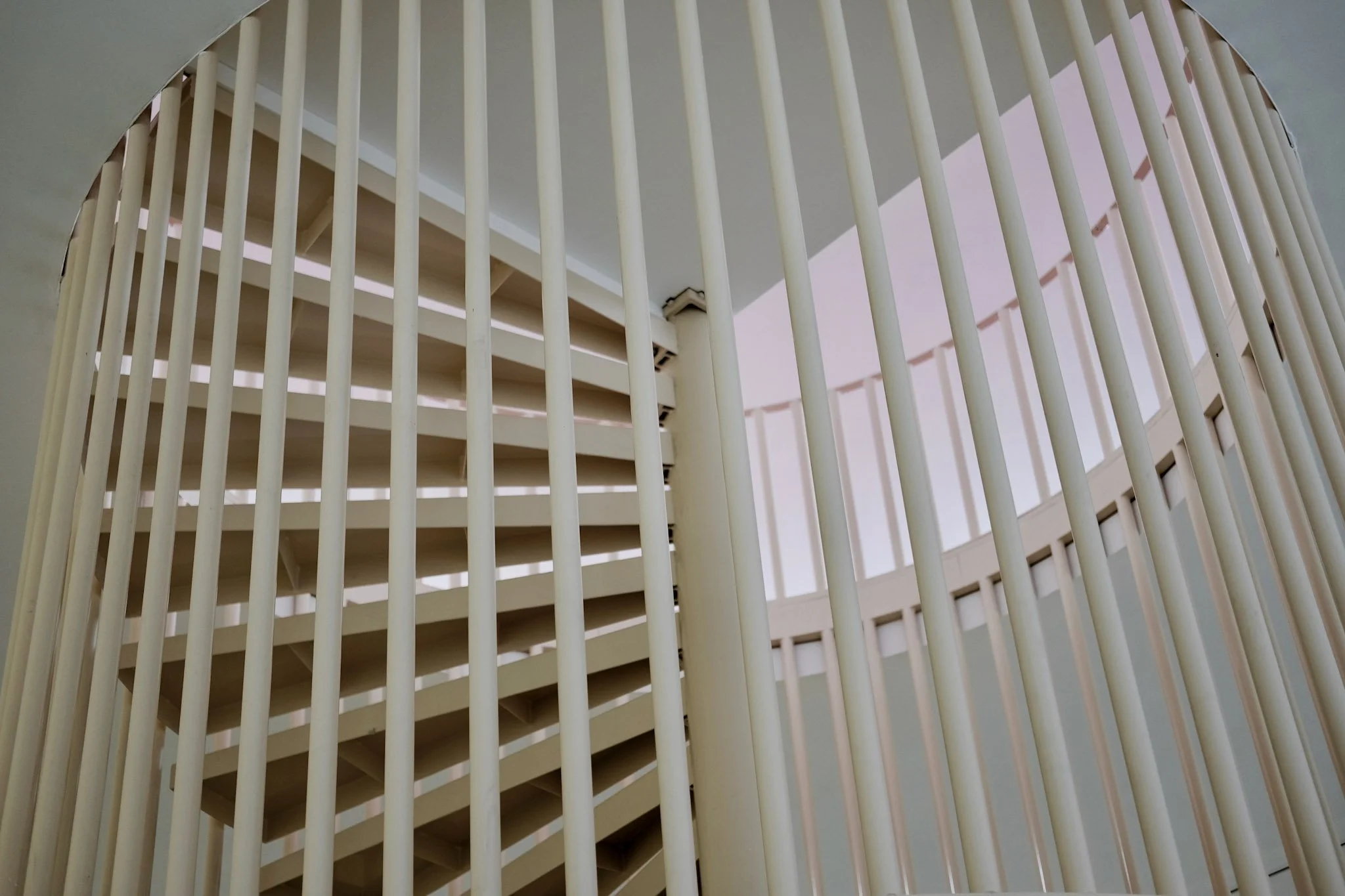 View of a modern staircase with vertical white balusters, viewed from below through a partial circular opening, with natural light illuminating the area.