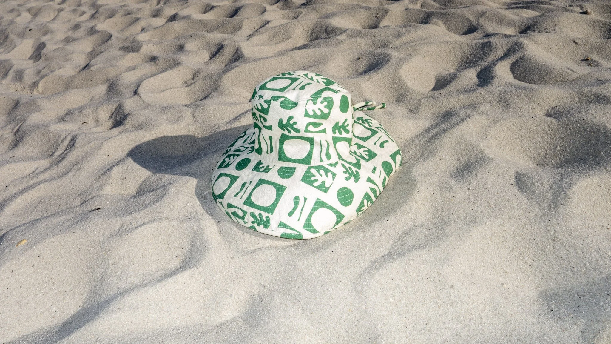 A hat with green and white abstract patterns sitting on sandy beach.
