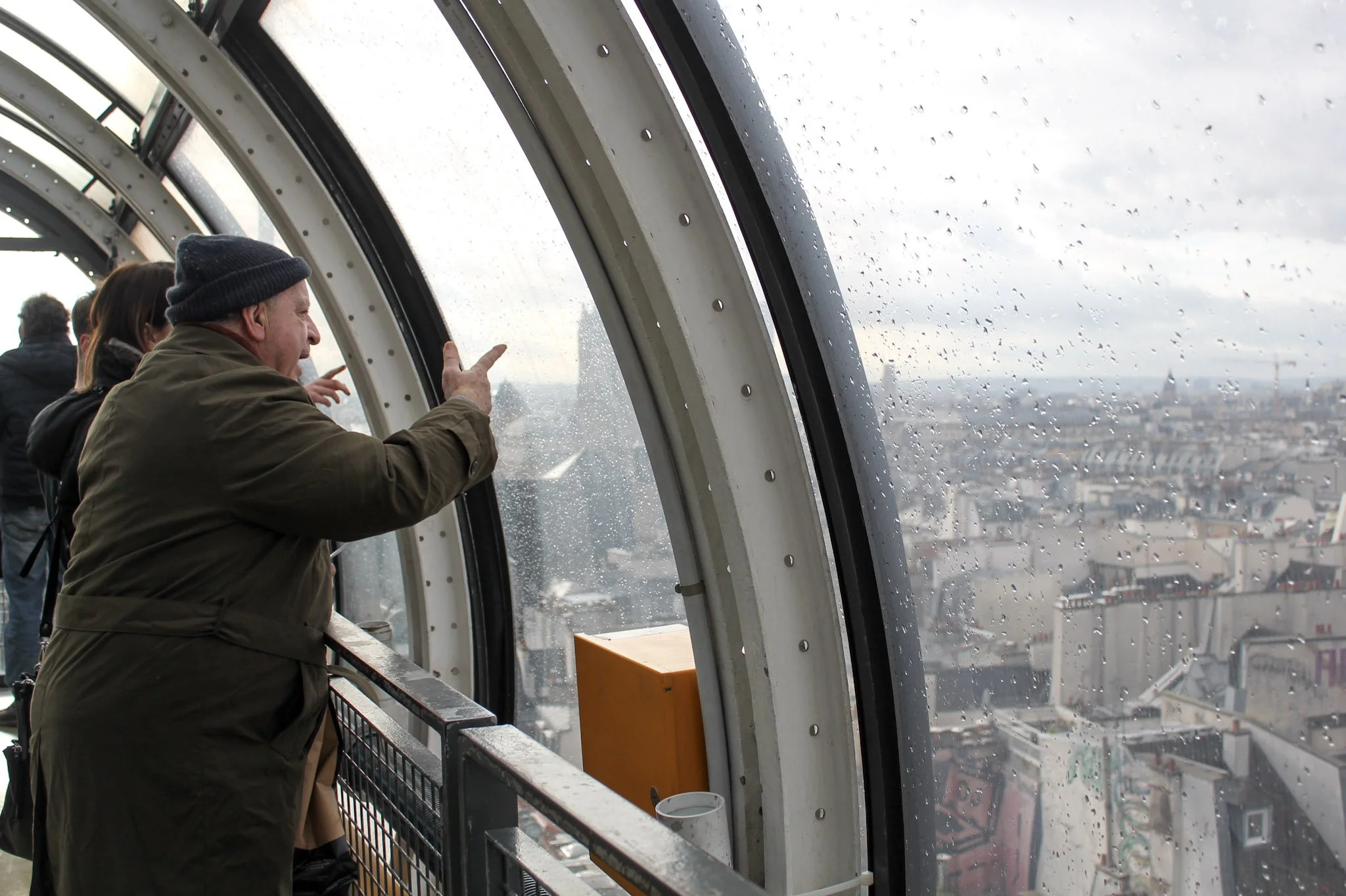 People observing the city from the top of the Eiffel Tower on a rainy day.