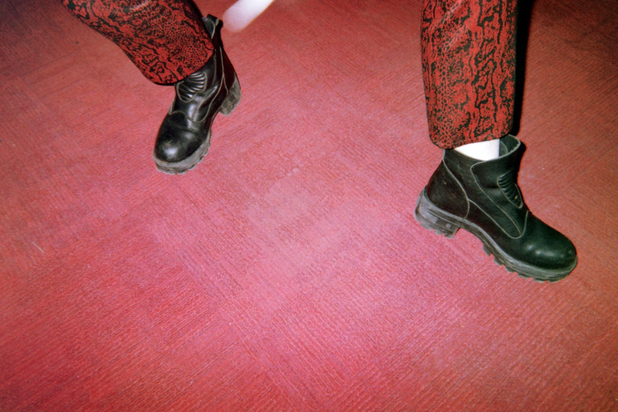 A person standing on a red carpet with black combat boots and red and black patterned pants.
