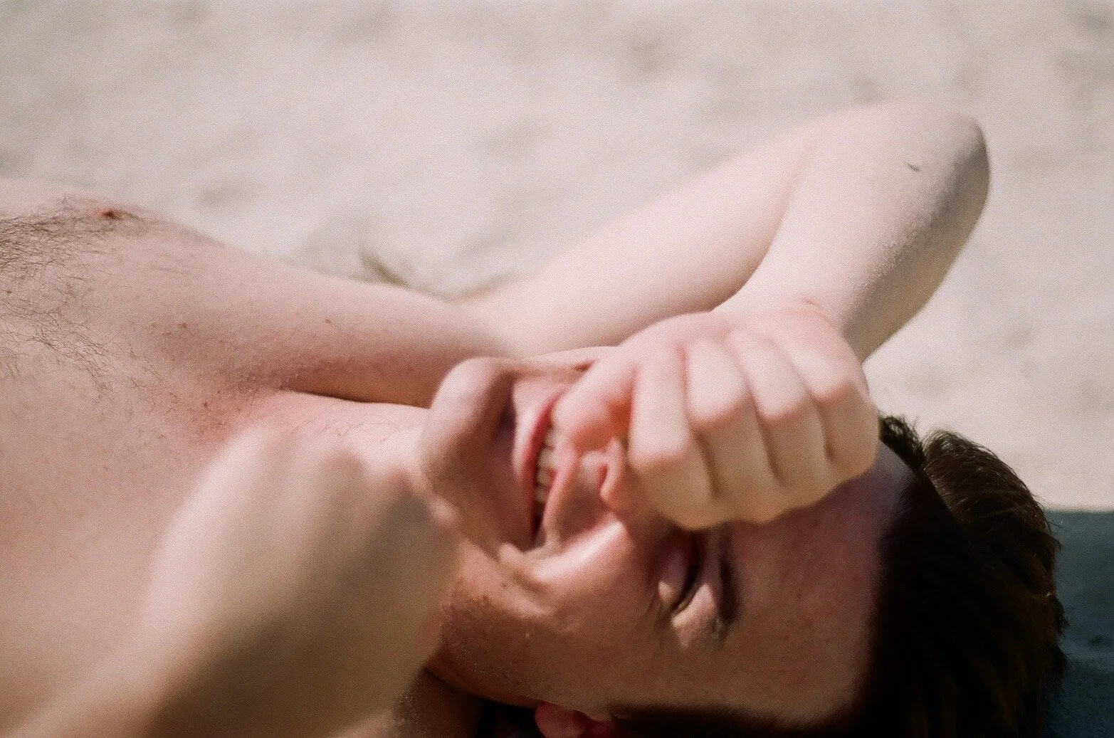 A person with dark hair lying on the sand, smiling and holding a large sex toy.