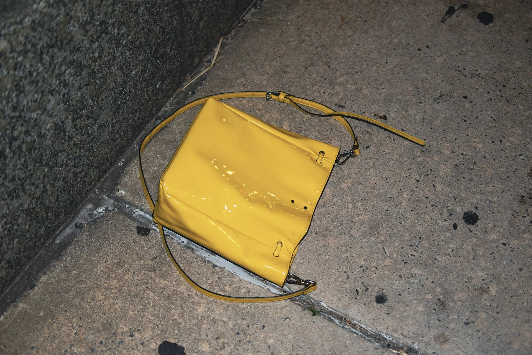 Yellow handbag resting on a sidewalk against a concrete wall.