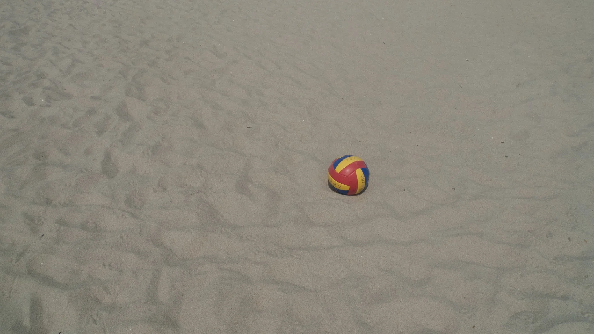 Colorful volleyball resting on sandy beach with footprints.
