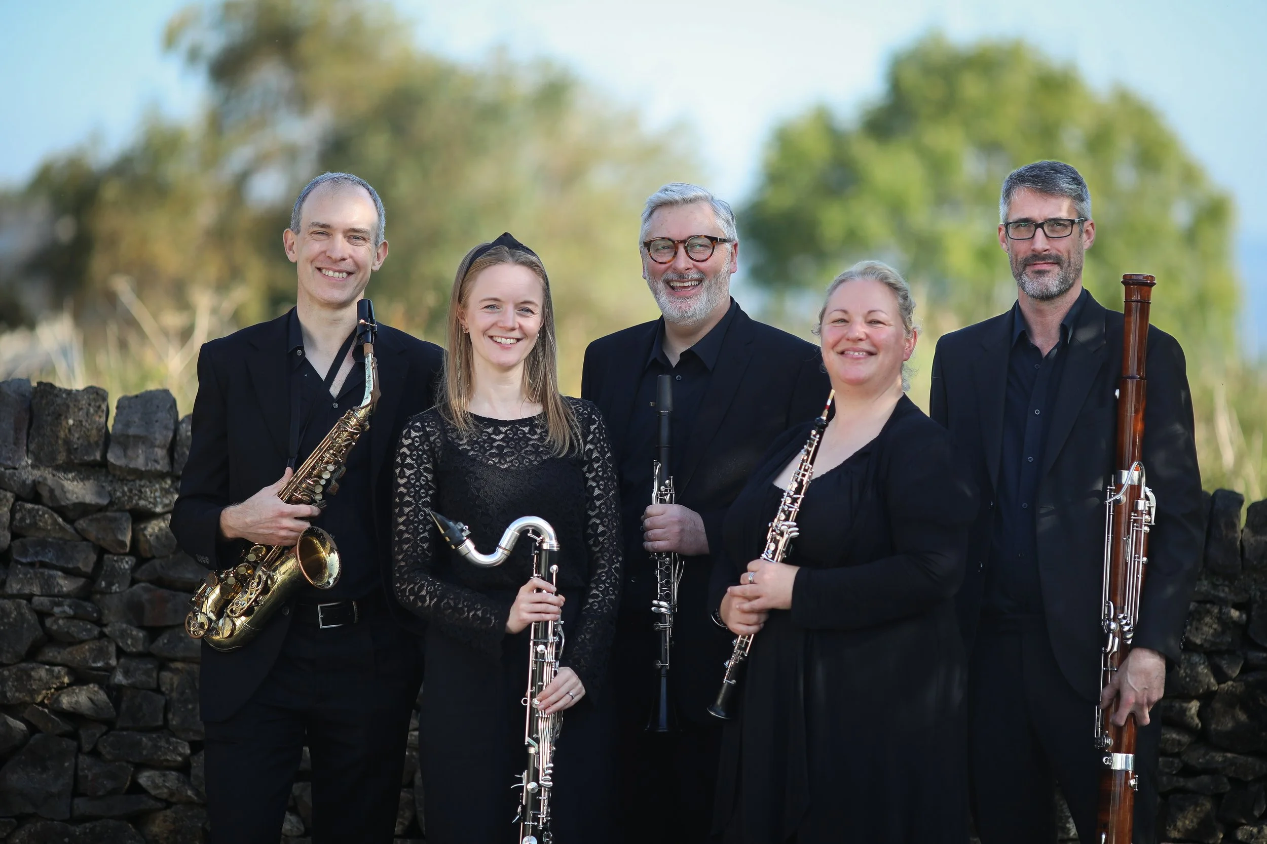Arundo5 reed quintet outdoors, smiling on a sunny day before a concert in the Peak Distict, with oboe, clarinet, saxophone, bass clarinet and bassoon.