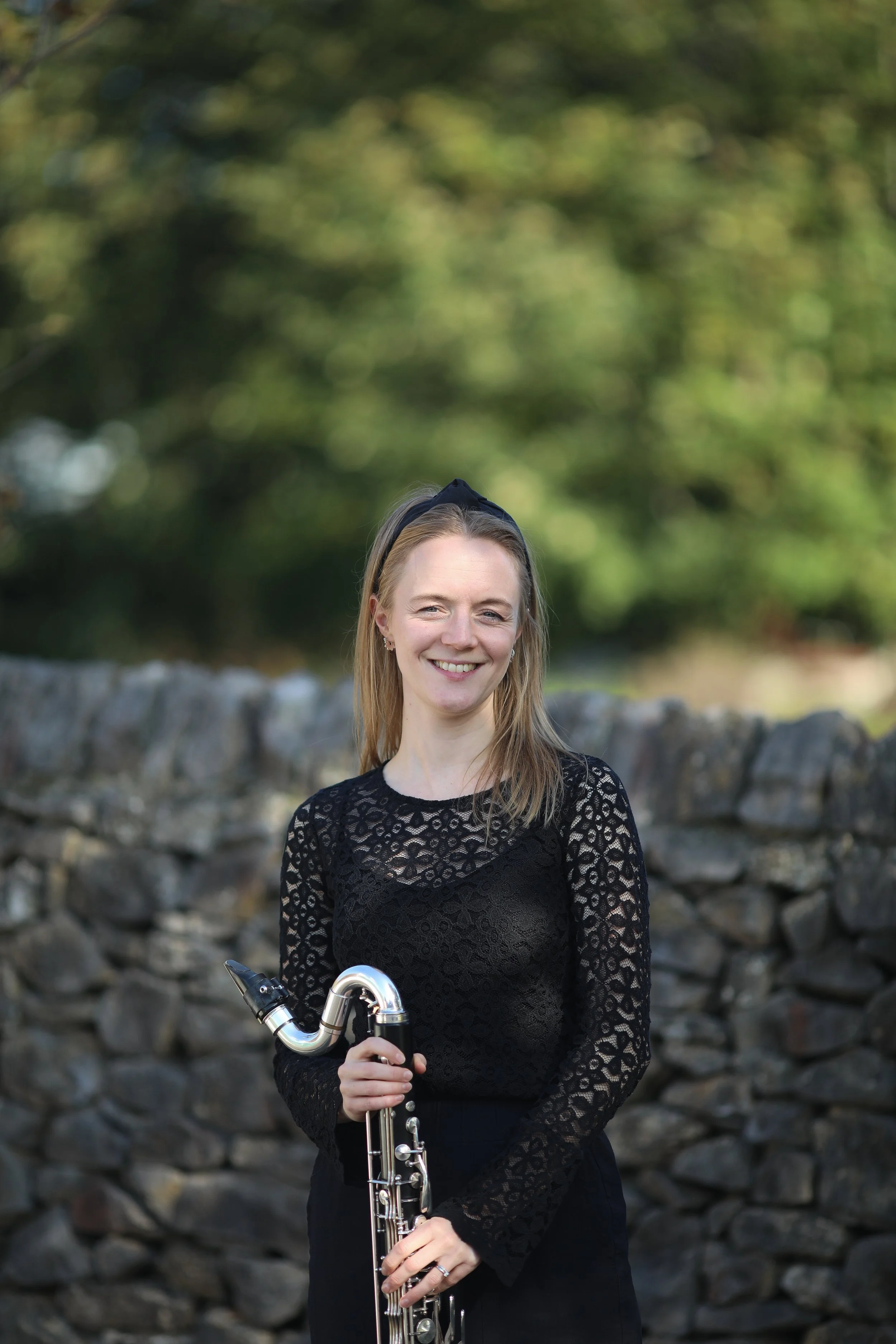 Jess, bass clarinet player with Arundo5, holding her bass clarinet outdoors.