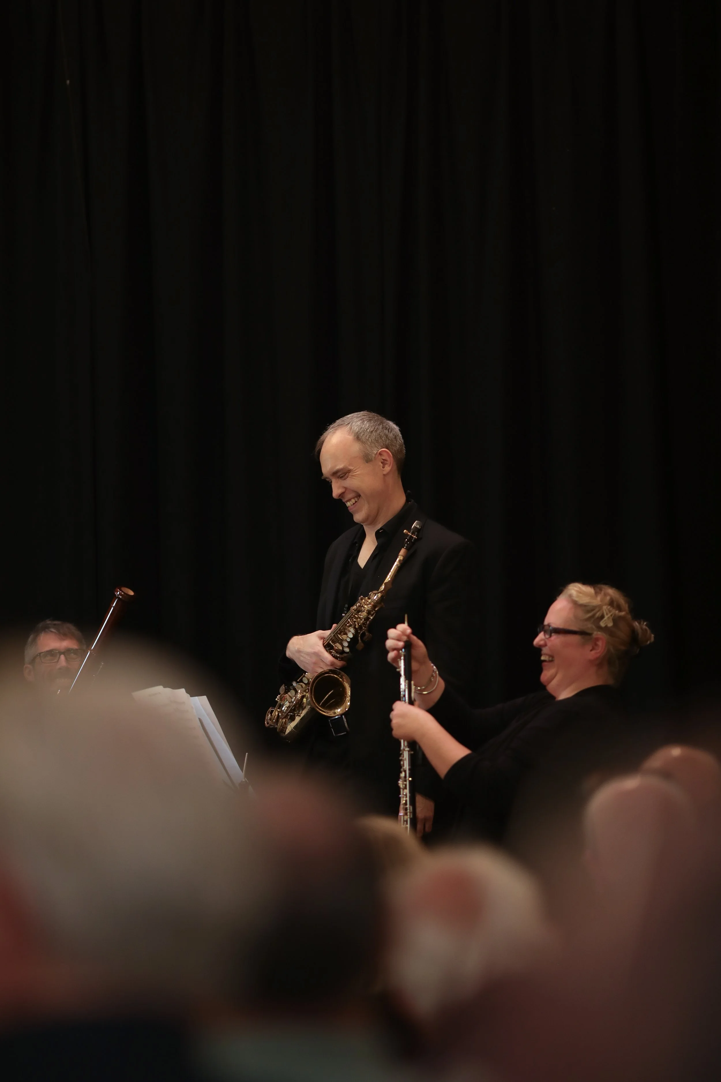 Arundo5 performing on stage, seen from the audience. Toby with his saxophone addresses the audience as Manon adjusts her reeds