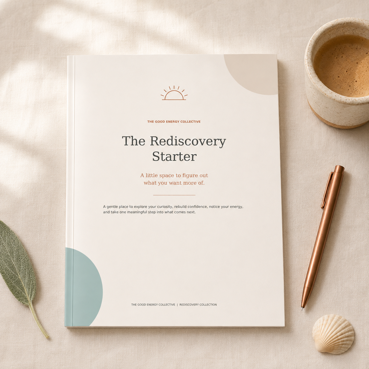 A white booklet titled 'The Rediscovery Starter' from The Good Energy Collective, with a sun icon, placed on a beige surface with a cup of coffee, a rose gold pen, a seashell, and a green leaf around it.