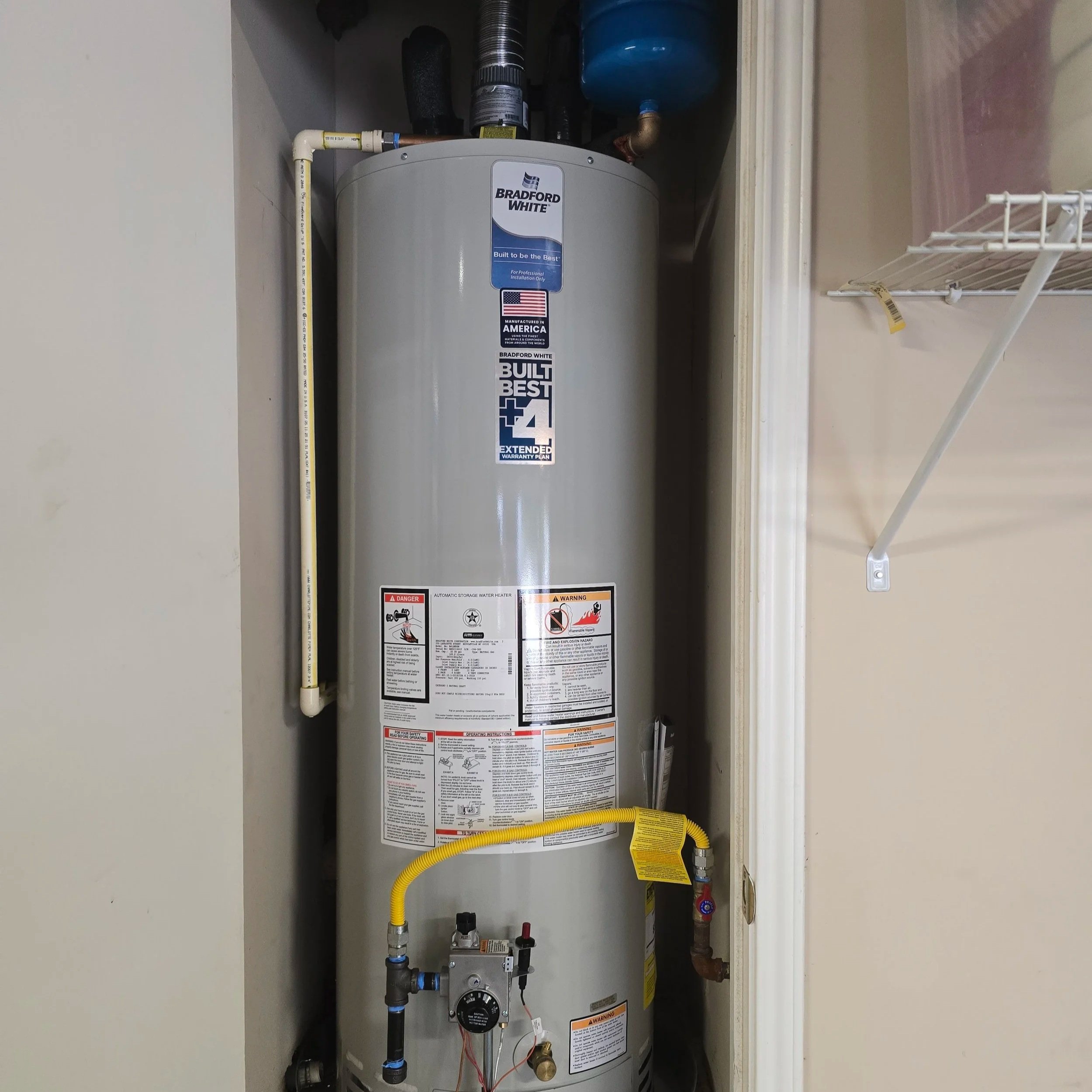 A water heater in a closet with various pipes and labels, including a Bradford White logo and warning stickers.