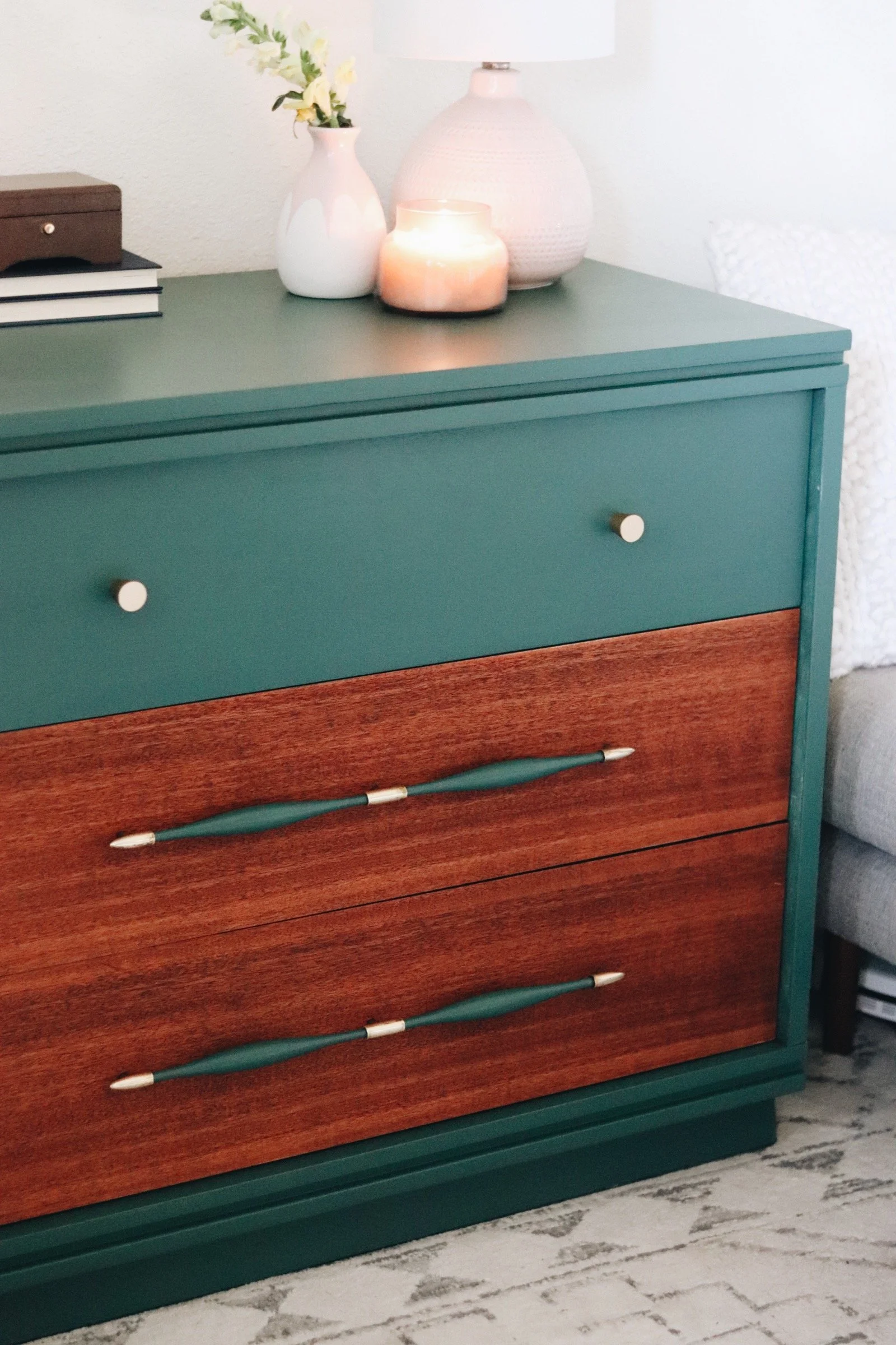 A dresser painted teal and wood with decorative finials on the drawer pulls, placed on a marble floor.