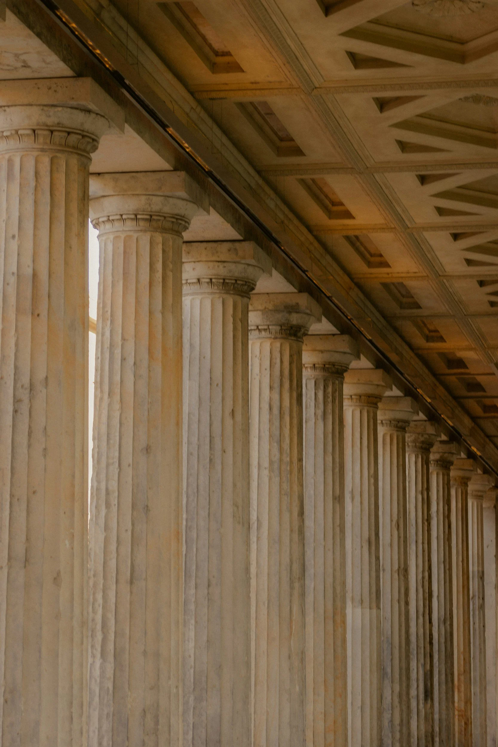 A row of marble classical columns with fluted shafts and ornate capitals, topped with a coffered ceiling with geometric patterns.