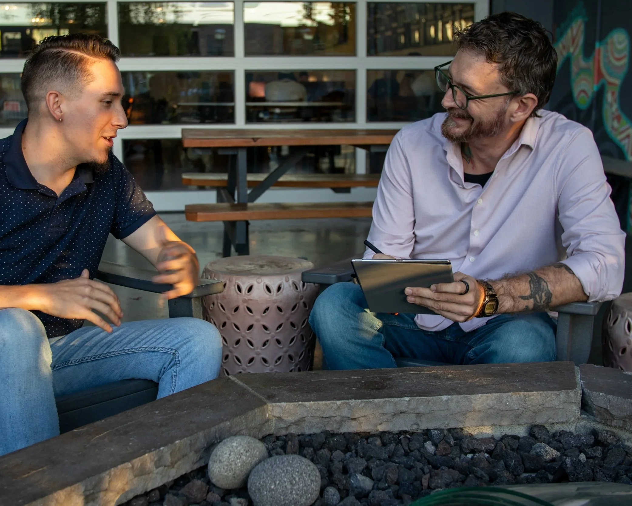 J. Michael Decker (Mikey) holding a tablet in conversation with a client, seated outdoors on a patio.