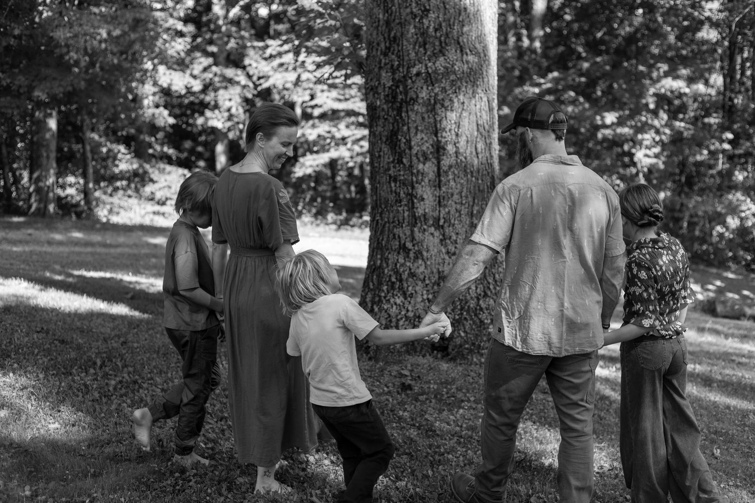 Black-and-white photo of Jenna walking hand in hand with her spouse and children beneath a large tree