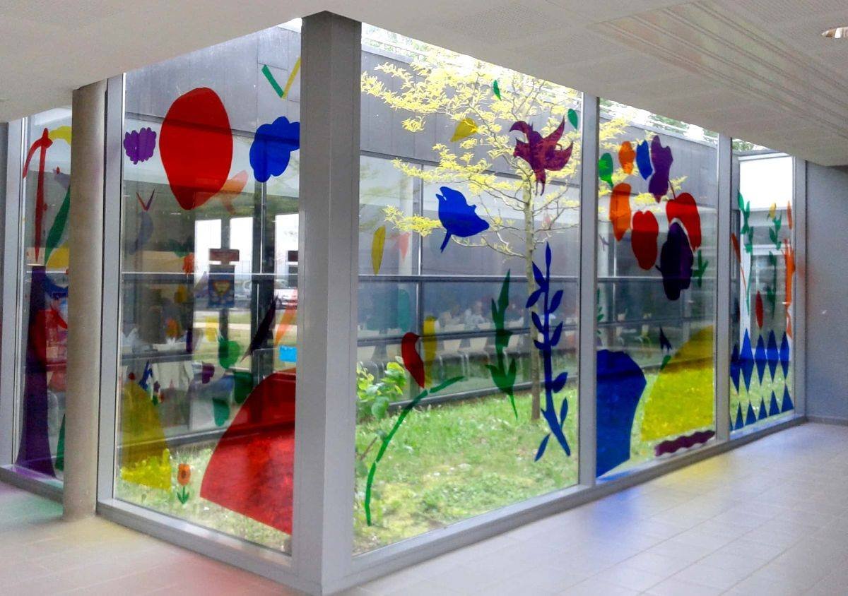 Baies vitrées décorées de motifs colorés représentant des fleurs et des formes abstraites dans un couloir lumineux.