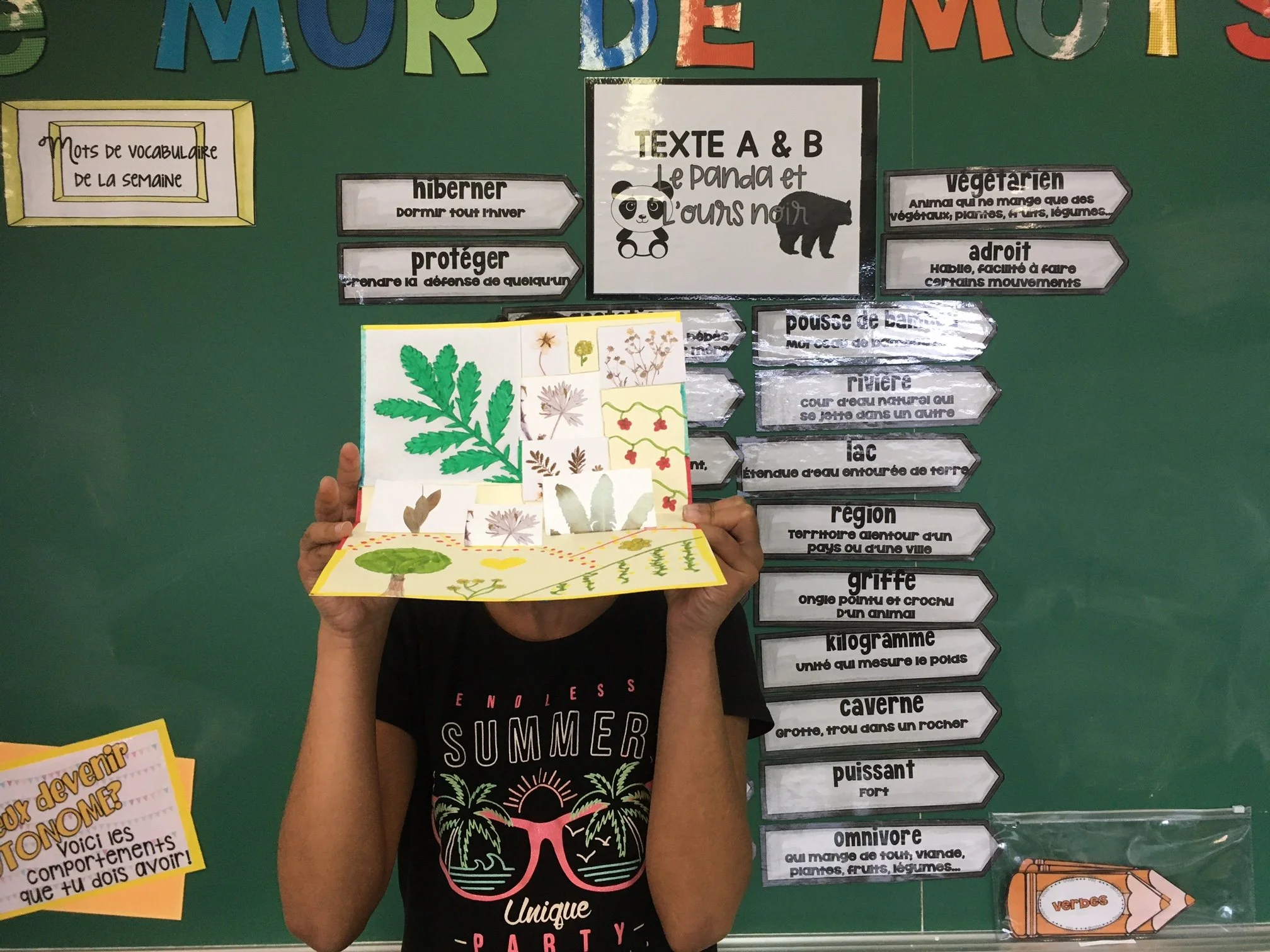 Tableau scolaire de vocabulaire français sur le thème de la nature, avec définitions, illustrations d’animaux et de plantes, et un élève tenant un herbier.