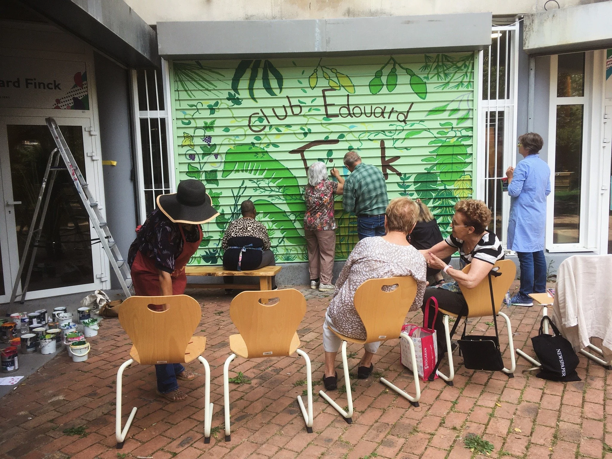 Groupe de personnes peignant une fresque végétale colorée sur un volet roulant extérieur.