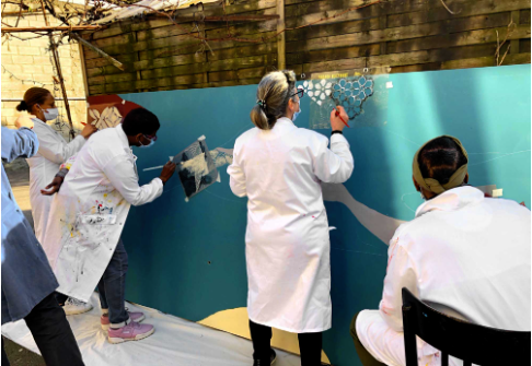 Artistes en blouse blanche peignant une fresque colorée sur un mur turquoise.