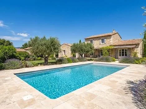Stone villa with terracotta roof and swimming pool surrounded by landscaped grounds under a clear blue sky