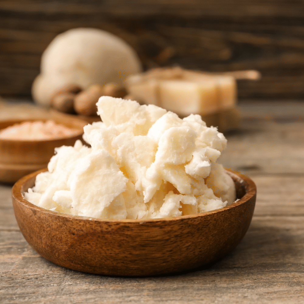 A bowl of mashed potatoes on a wooden surface with garlic, ginger, and cheese in the background.