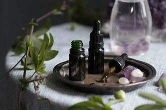 Essential oil bottles, a dropper, and crystals on a tray, with a glass of water and greenery in the background.