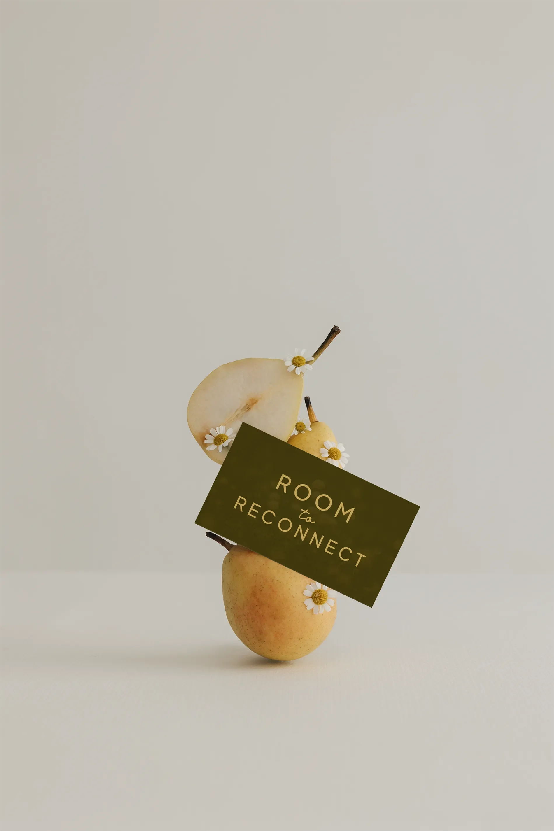 Three pears with small white daisies on top and a black card that reads, 'Room to reconnect' against a plain white background.