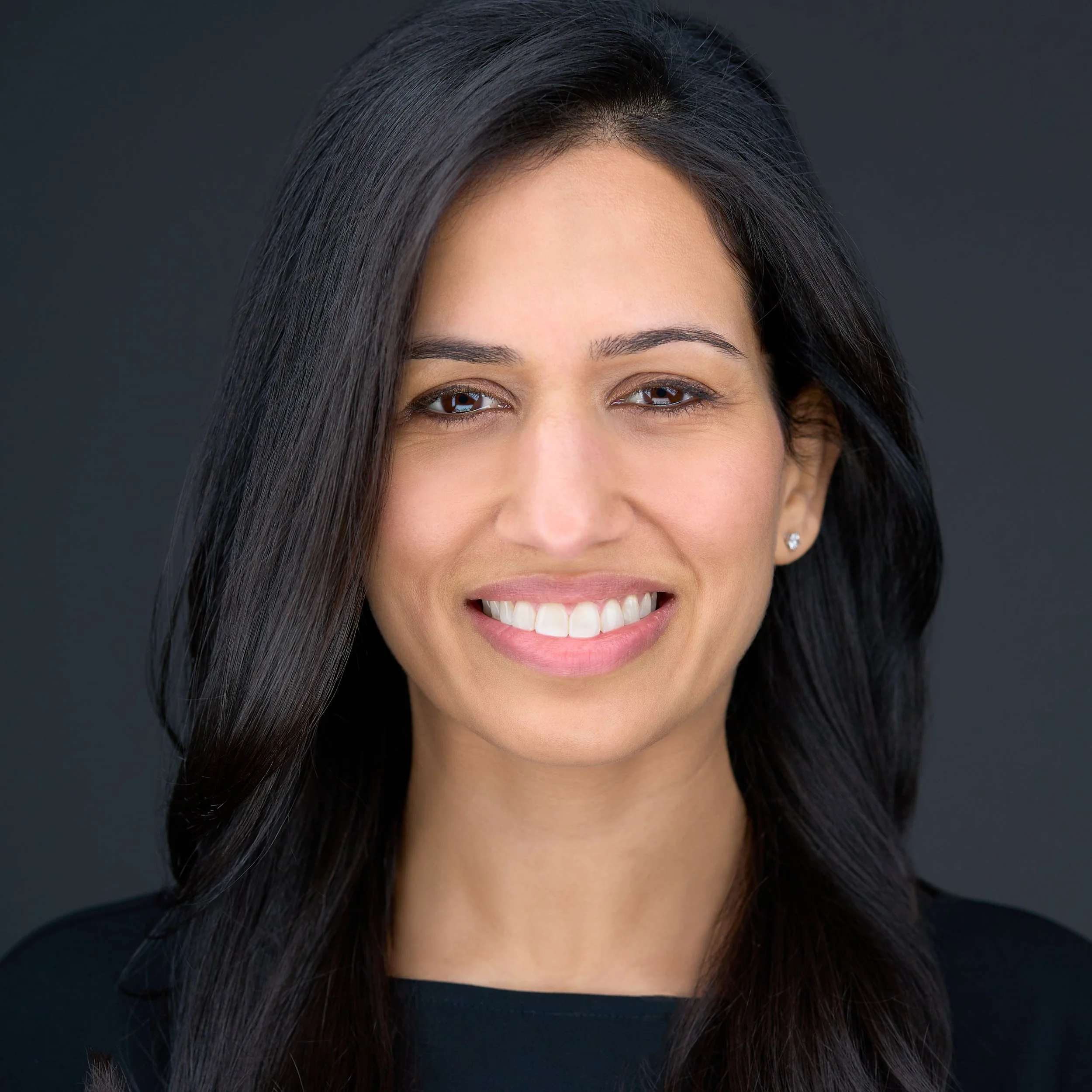 DAVIDSAGGIO Photography Tampa female entrepreneur portrait. Smiling and looking directly at the camera. Wearing black top against a dark gray background.