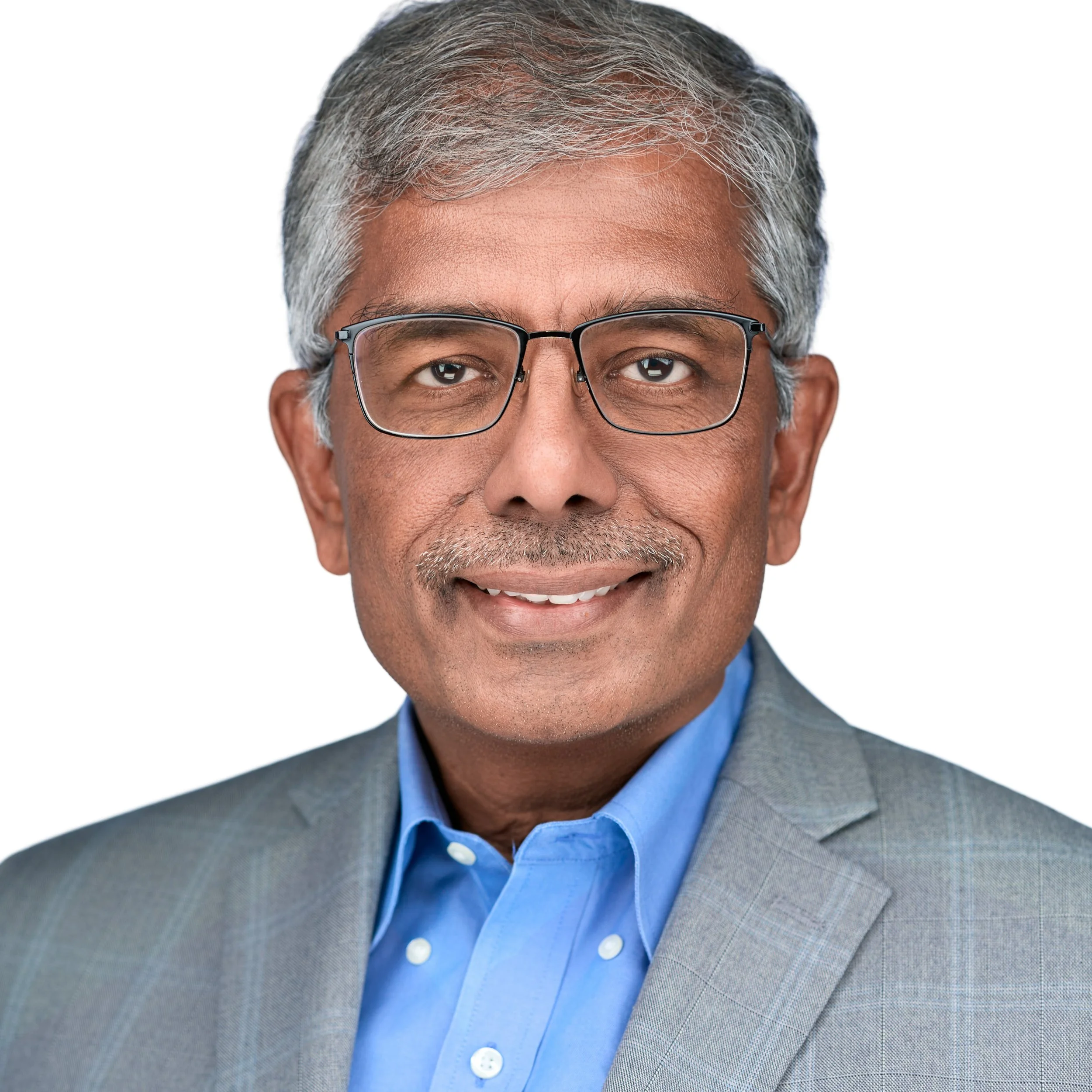Indian male executive headshot. Graying hair, glasses, smiling and wearing a blue button down, and gray jacket on white background. DAVIDSAGGIO Photography Tampa