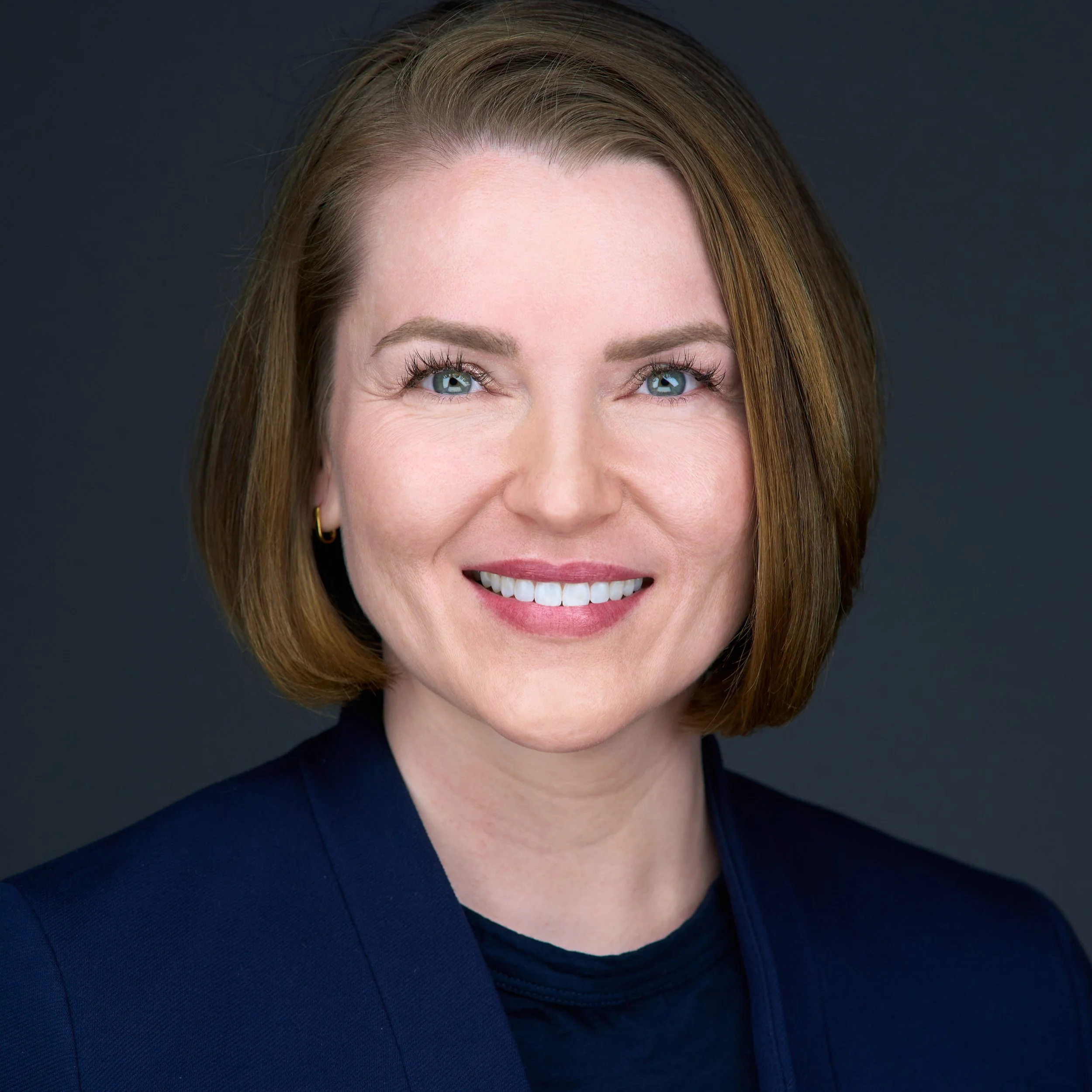 DAVIDSAGGIO Photography Tampa female healthcare executive leadership portrait. Happy smile with bright blue eyes. Ginger hair wearing black top and navy jacket. Dark background.