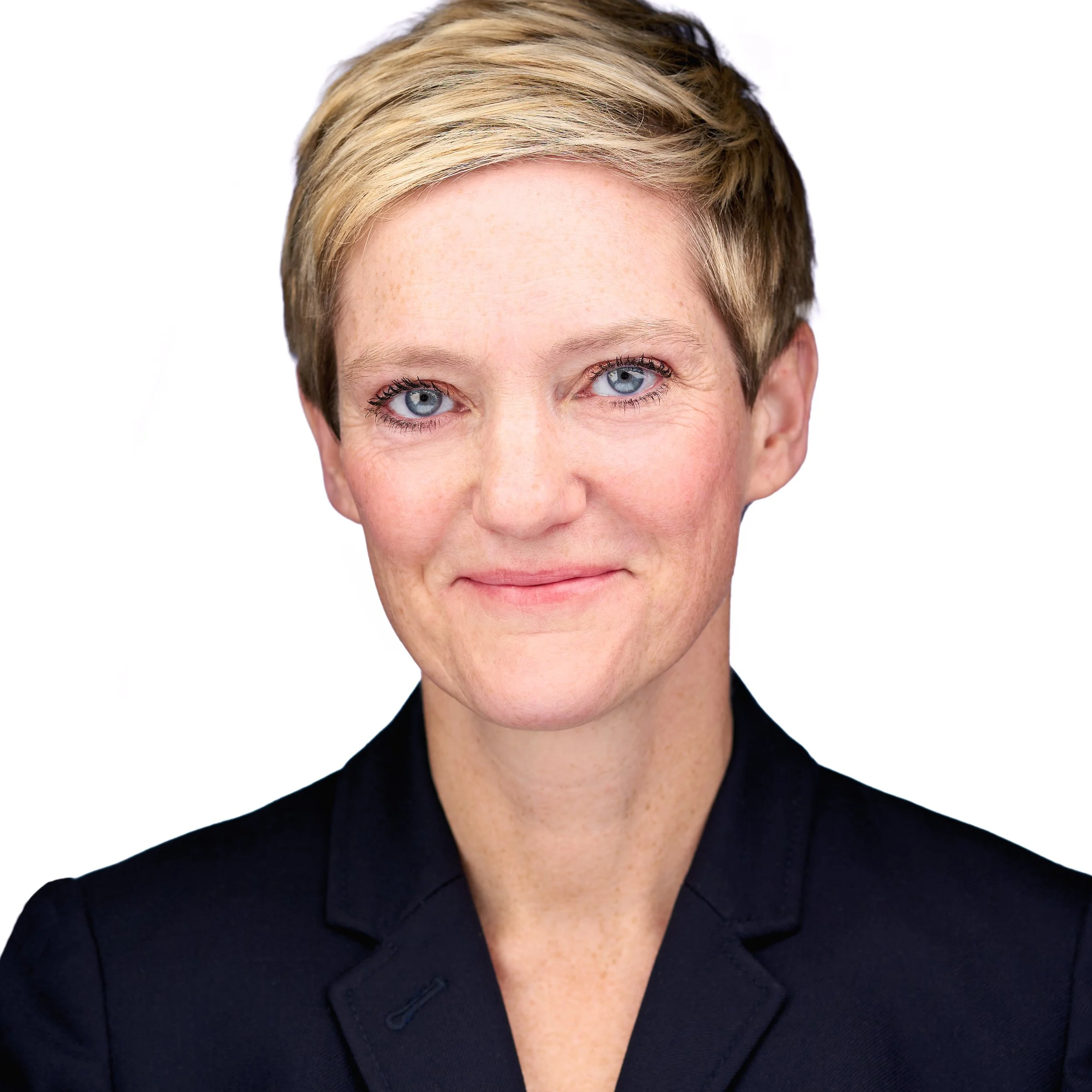 DAVIDSAGGIO Photography Tampa female executive headshot. Blonde with closed mouth smile and bright blue eyes. Wearing a black jacket against a white background.
