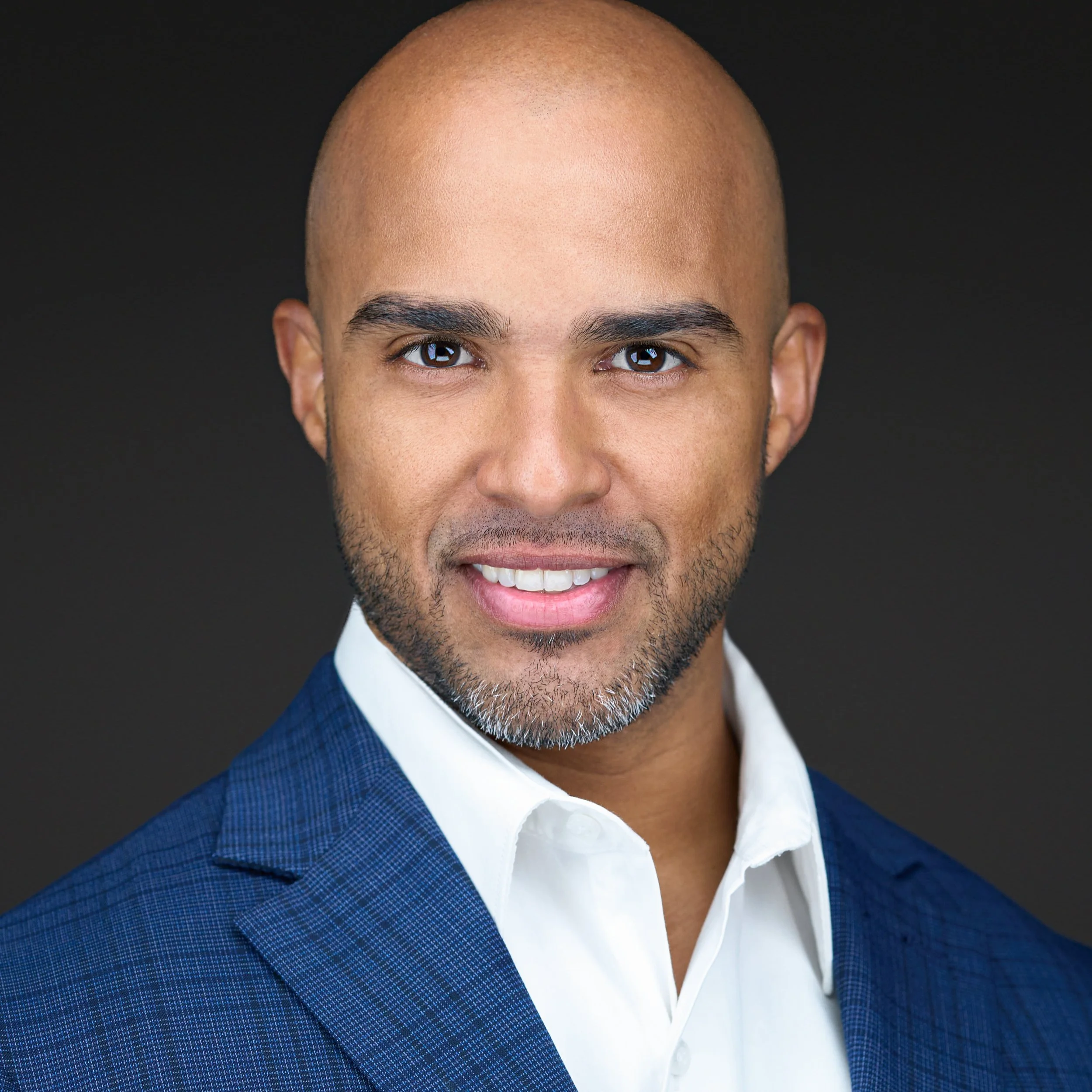 DAVIDSAGGIO Photography Tampa hispanic male entrepreneur portrait. Turned to side. Wearing white button down, blue jacket against a dark gray background.