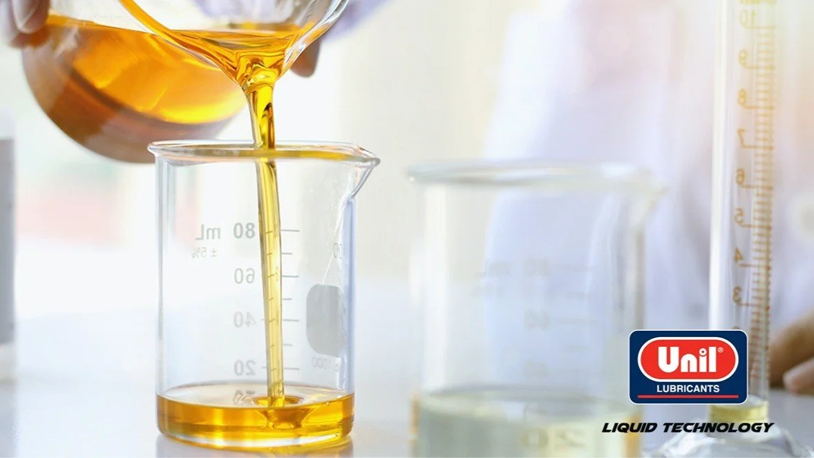 A beaker with yellow liquid being filled from a flask, with laboratory glassware and a Unil lubricants logo in the background.