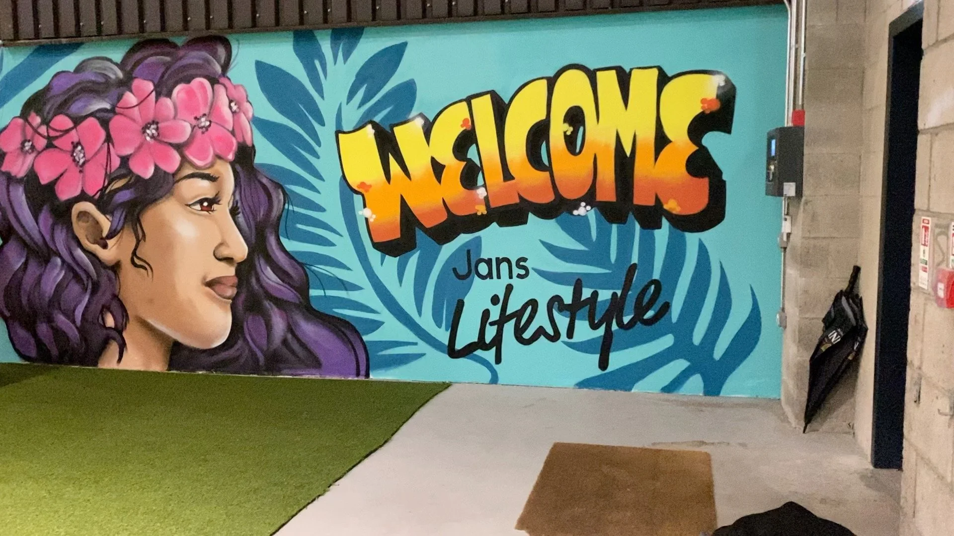 A colorful graffiti mural featuring a woman with purple hair and pink flowers in her hair, alongside the text 'Nescafé Lifestyle' on a blue background with palm leaves.