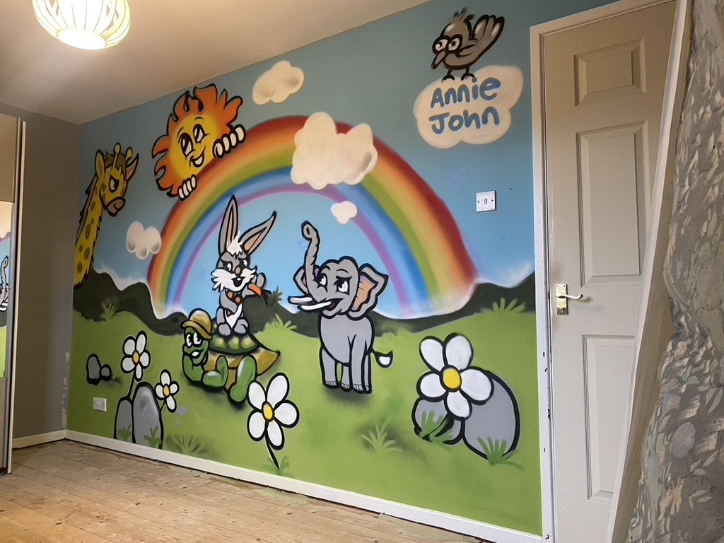 Colorful mural of cartoon animals and a rainbow painted on a wall, featuring an elephant, a rabbit, a giraffe, a lion, a bird, a turtle, and flowers, with a section labeled "Annie John".