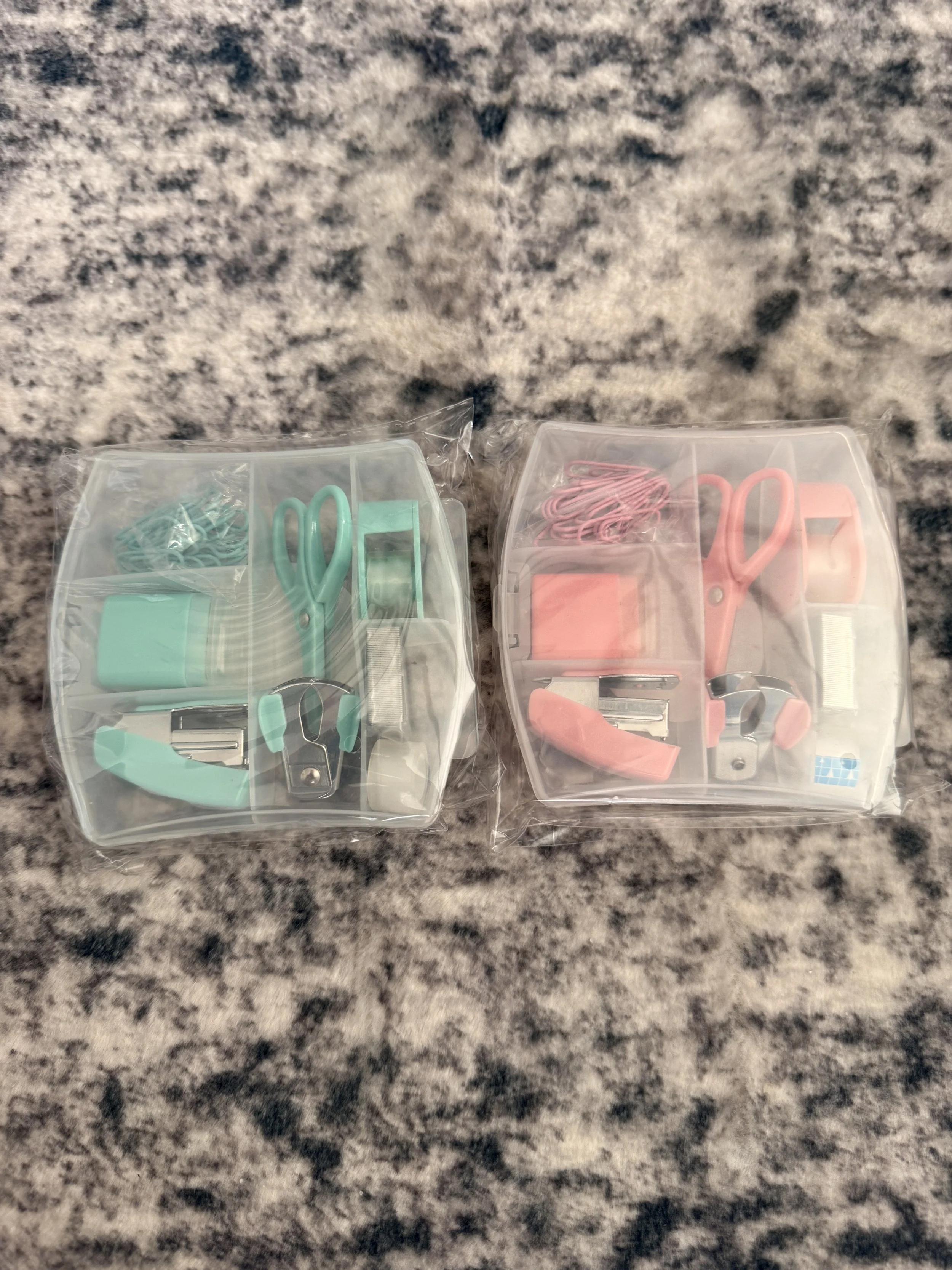 Two plastic organizer containers on a granite countertop, each containing sewing or craft supplies including scissors, clips, and other small tools.