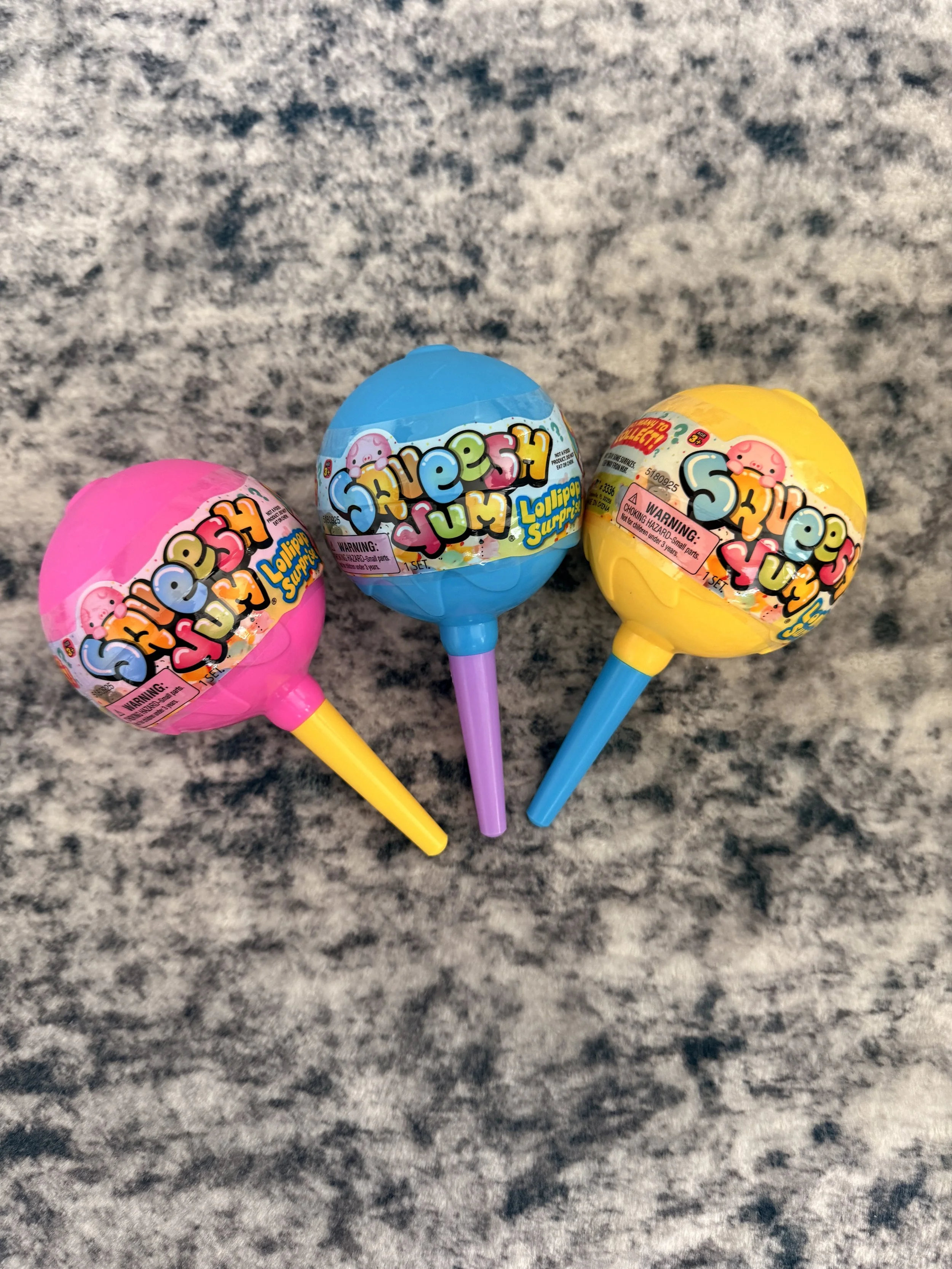 Three colorful slime surprise eggs with plastic sticks, pink, blue, and yellow, lying on a granite countertop.