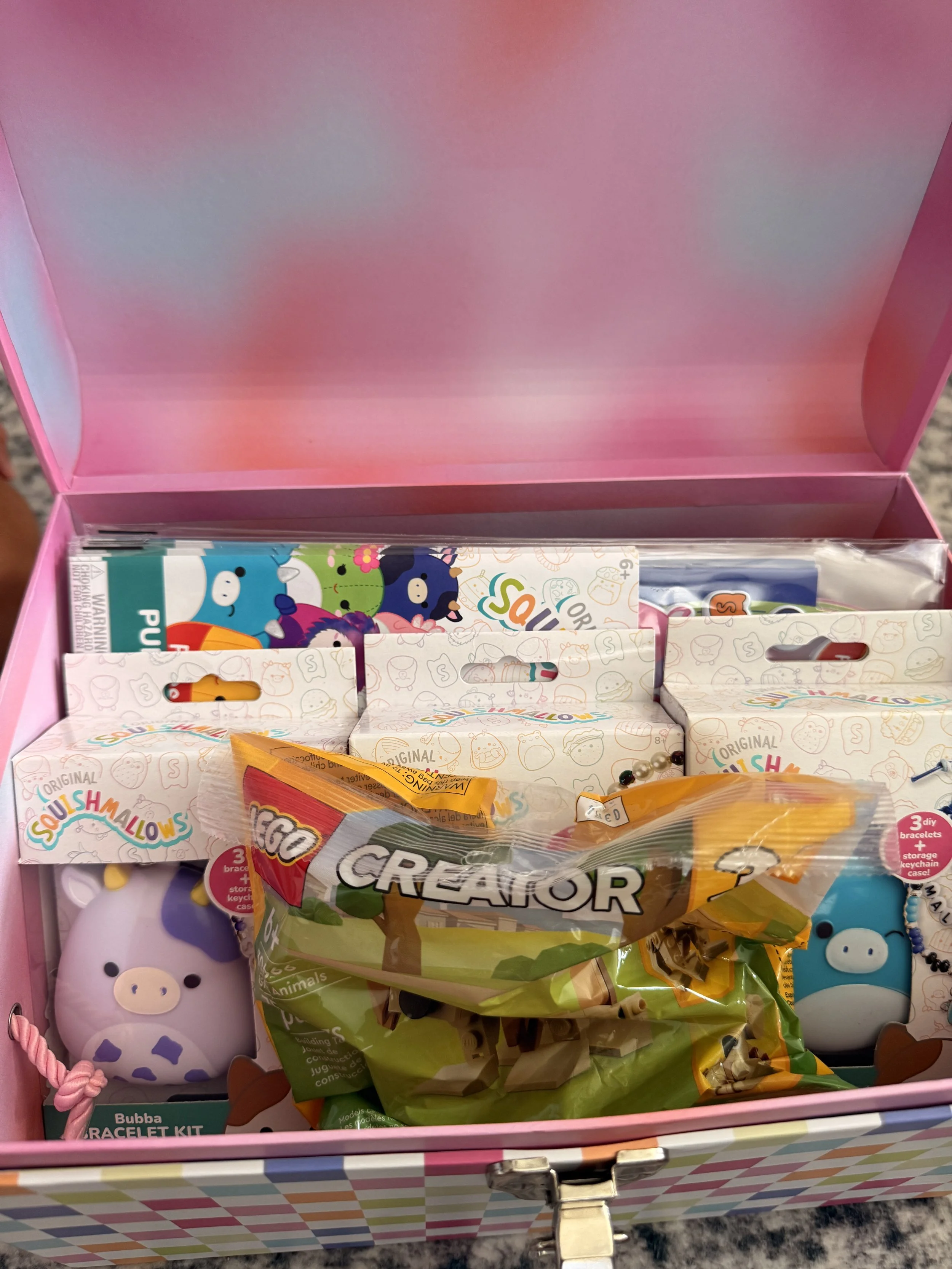 The image shows an open pink box containing various slime-related toys and accessories, including squishy toys, slime kits, and slime molds.