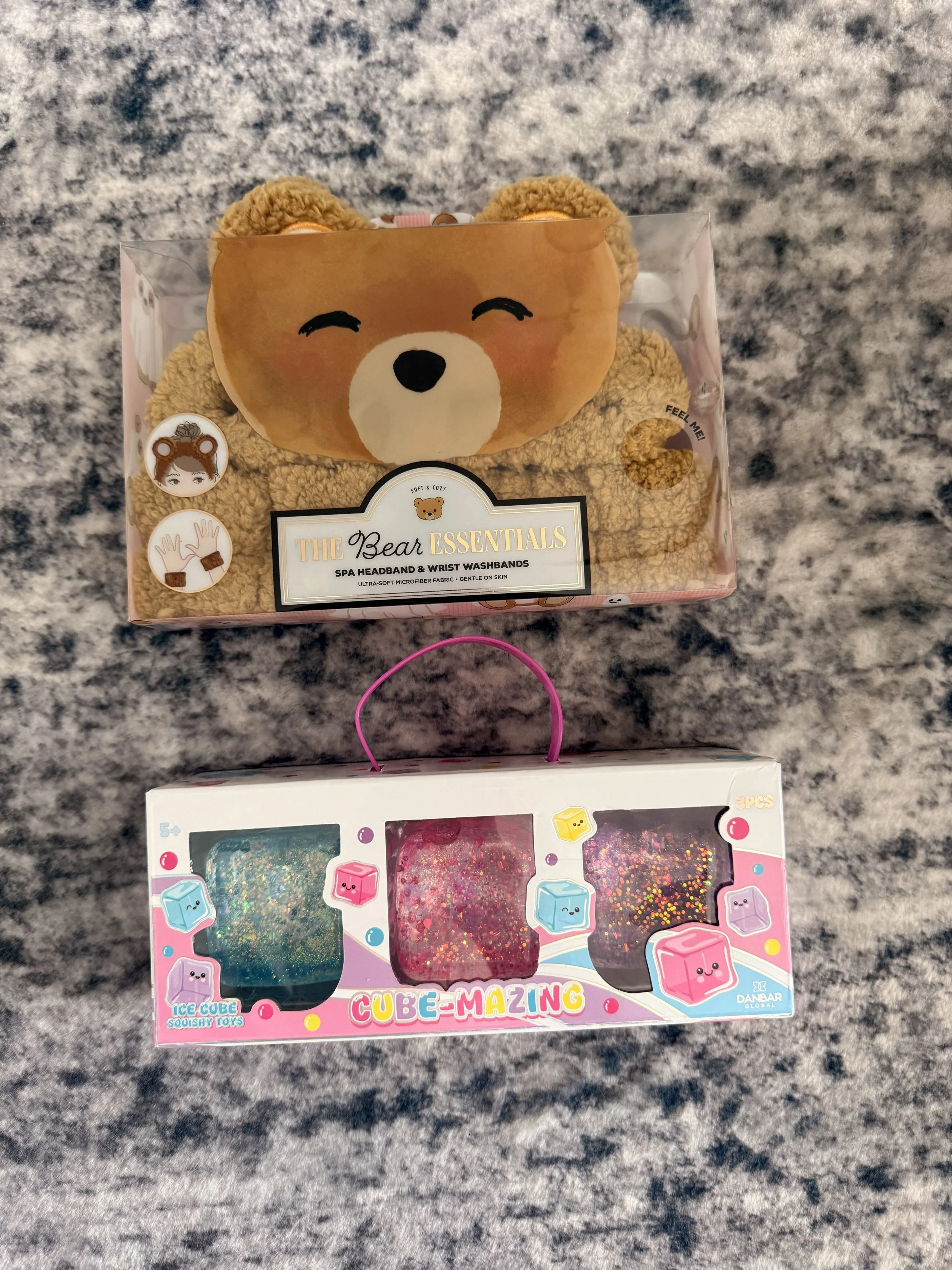 A boxed set of a bear-themed headband and wrist washables on a marble surface, with a separate box of colorful squishy toys visible below.