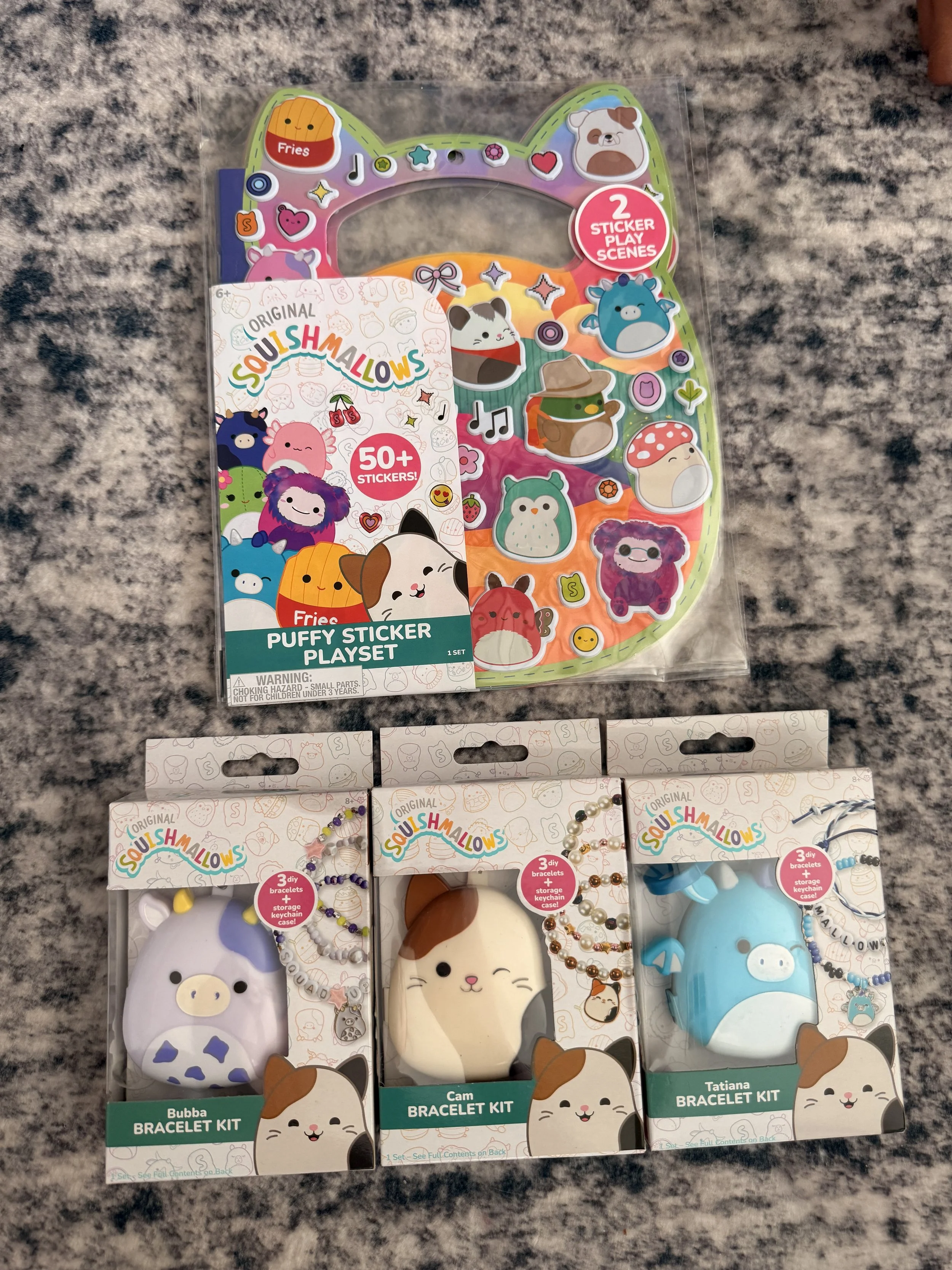 A collection of Squishmallows-themed baking and jewelry kits in colorful packaging, including bracelet kits with various designs, a pancake kit, and a bracelet kit with a cat design. The packages feature cartoon animal characters and colorful illustrations.