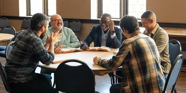 Five men sitting around a round table in a well-lit room, engaged in conversation and discussion.