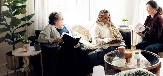 Three women sitting in a living room, reading books and chatting.