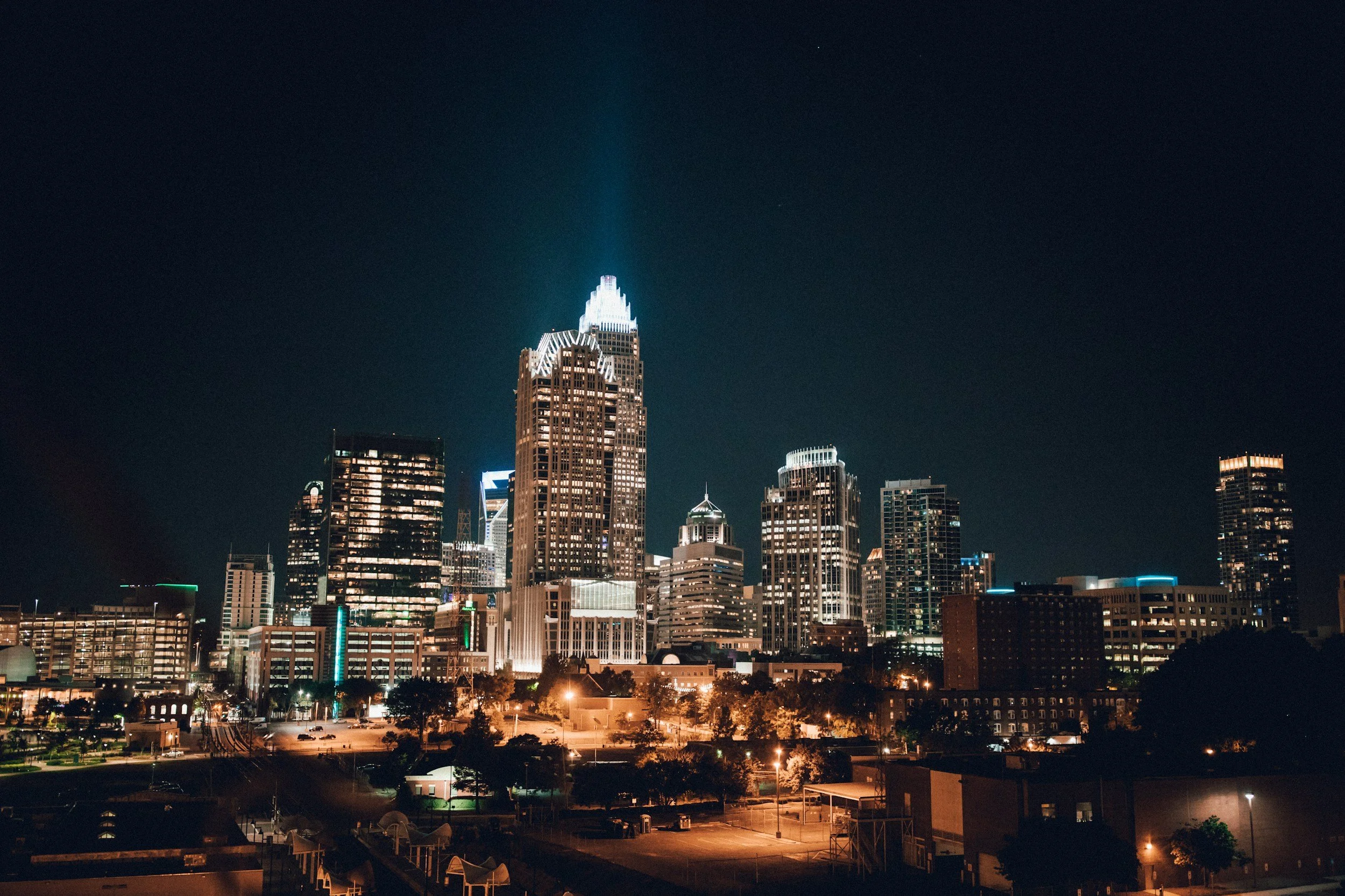 Nighttime city skyline with tall illuminated skyscrapers and buildings against a dark sky.