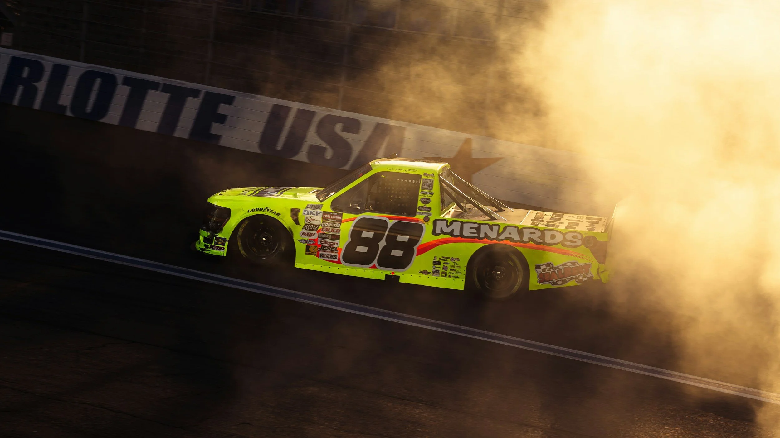 A neon green race car with the number 88 speeding around a track, with flames and smoke in the background and a wall with the word 'ROUTE US'.